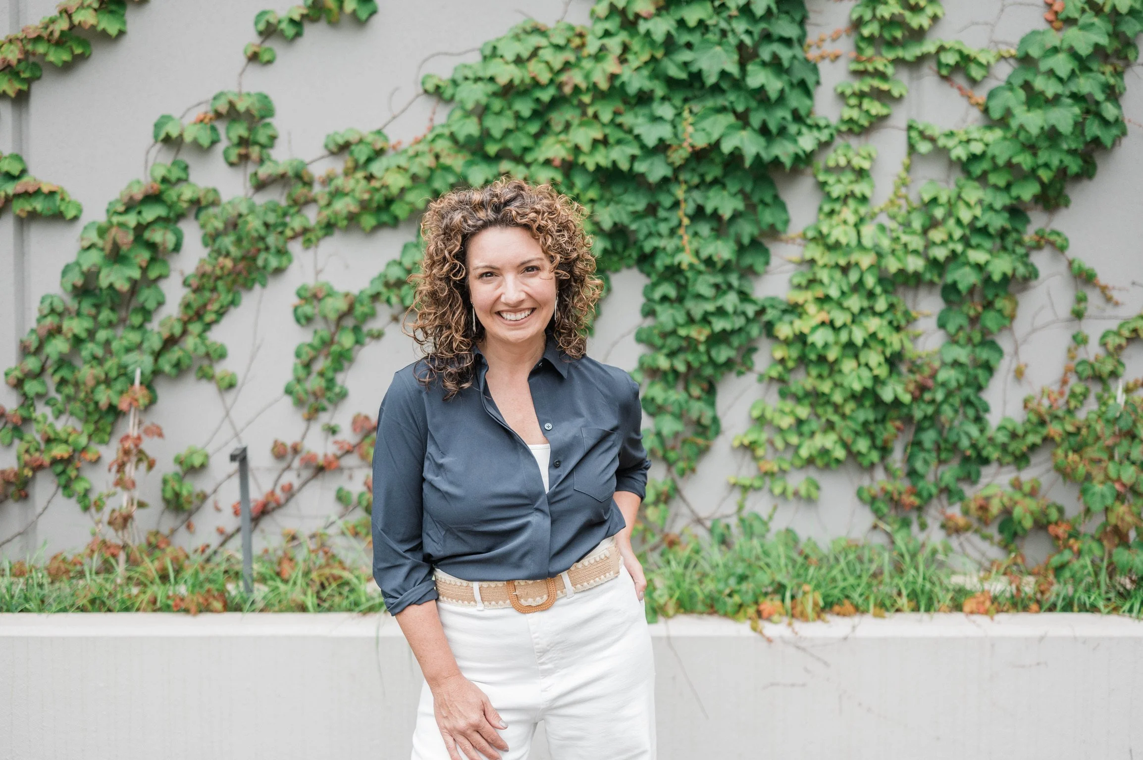Betsy Manley, luxury interior designer and renovation expert, standing outdoors against an ivy-covered wall.