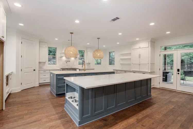 Renovated luxury kitchen featuring a large blue-gray island, white countertops, woven pendant lights, custom cabinetry, and warm hardwood floors.