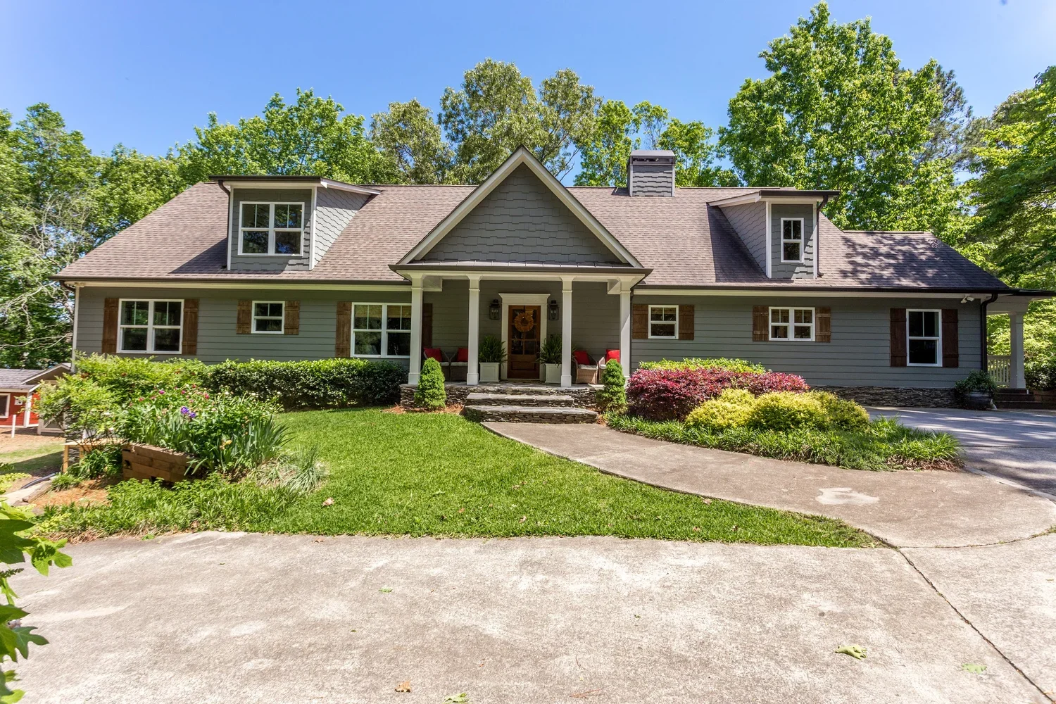 Renovated Lake Allatoona home exterior featuring gray siding, a welcoming covered porch, stone details, and lush landscaping.  I prefer this response