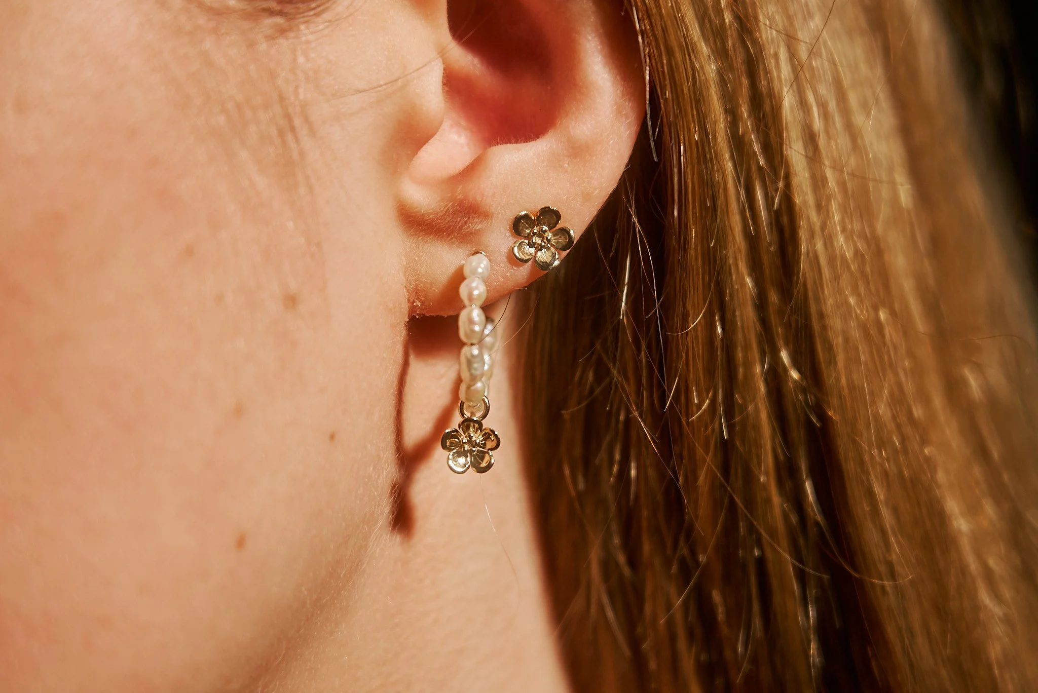 Freshwater pearl hoop earrings with 9ct gold forget-me-not charm worn alongside matching gold forget-me-not stud earrings.