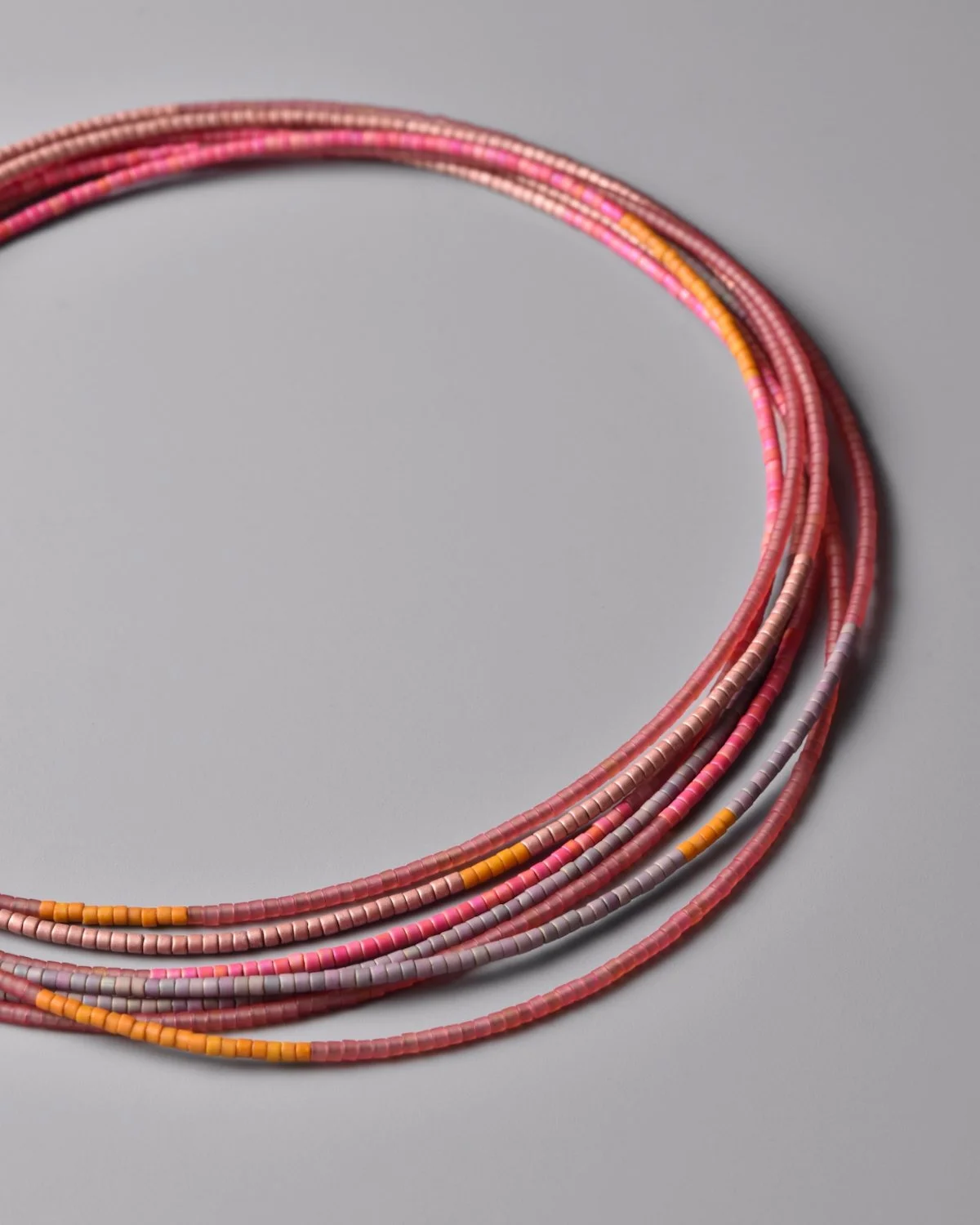 Hibiscus Sweep Necklace — close-up flat-lay detail of fuchsia, lavender, pink, and yellow Japanese glass bead strands on a grey background