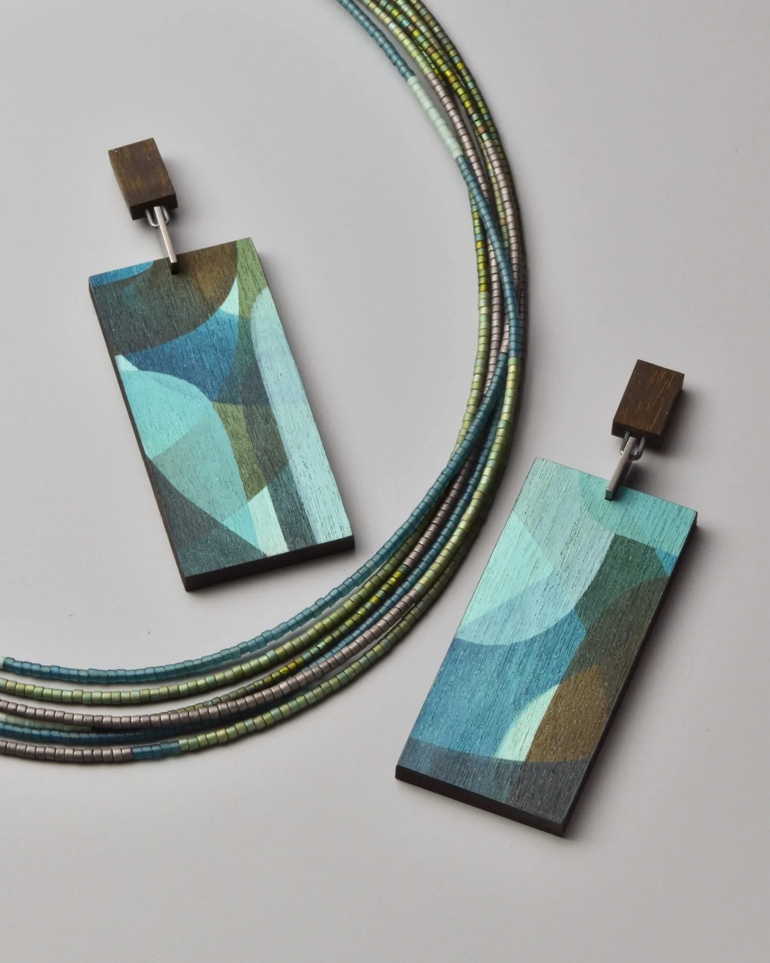 Arbor Sweep Necklace and Vela Earrings — close-up flat-lay detail of the forest-toned Japanese glass bead strands on a grey background