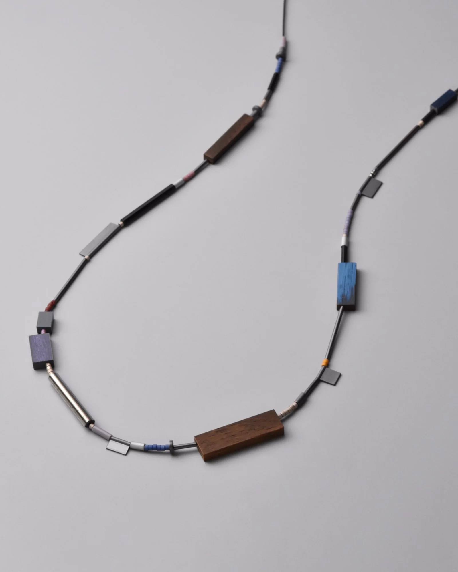 Devin Necklace — close-up flat-lay detail of mixed oxidized silver, vintage steel beads, glass beads, and walnut and eggplant maple elements on a grey background