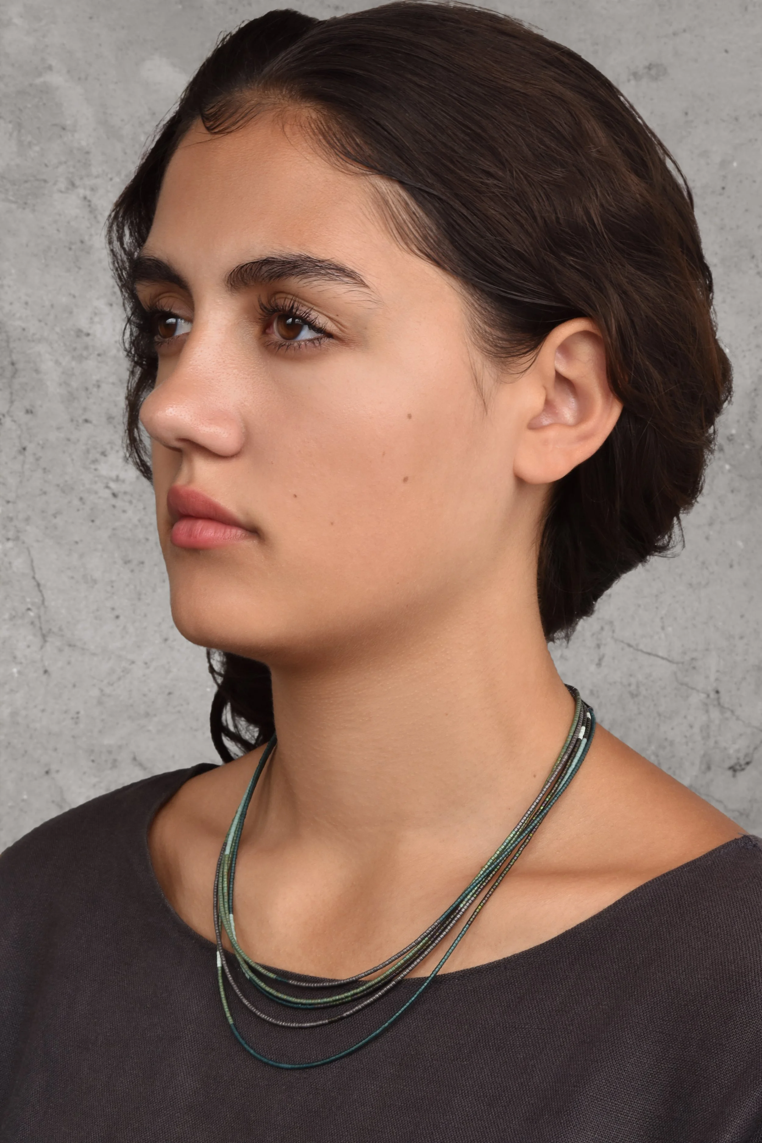 Arbor Sweep Necklace — worn by a model at a 3/4 view against a grey concrete background, the forest-toned beaded strands layered at the neckline