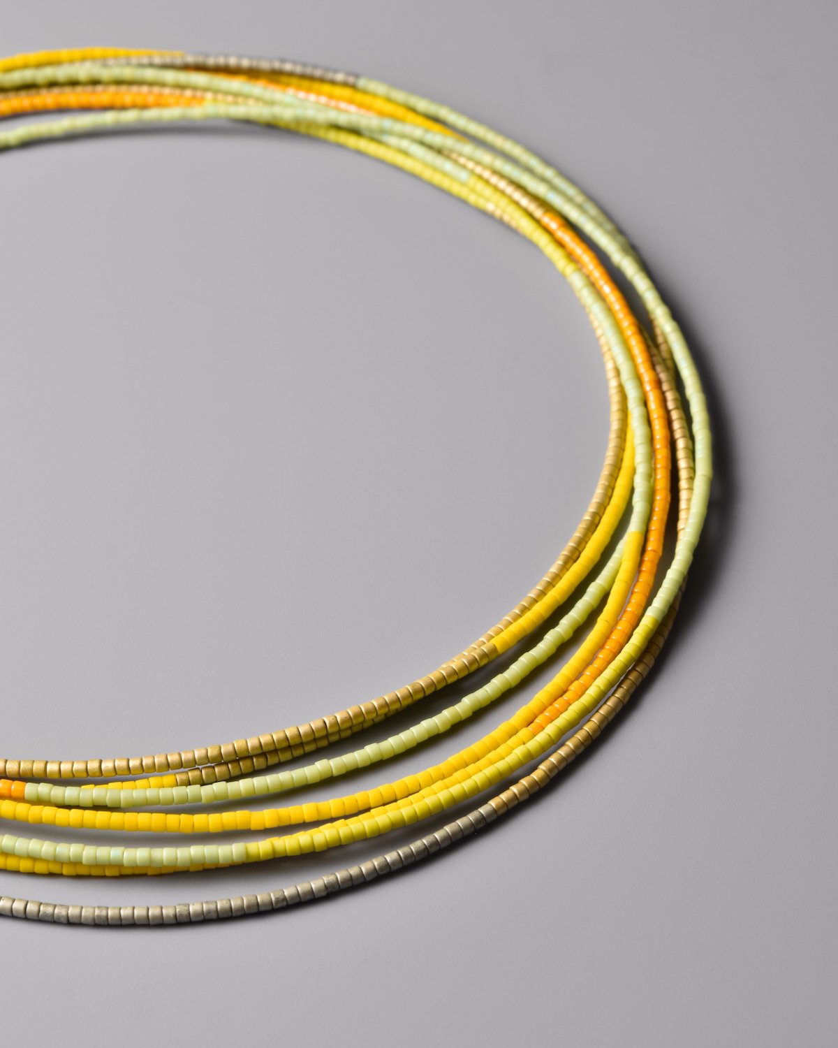 Citron Sweep Necklace — close-up flat-lay detail of the yellow-green Japanese glass bead strands on a grey background