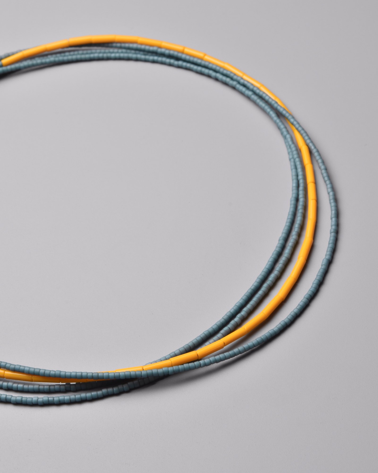 Cleo Necklace — close-up flat-lay detail of the soft blue and warm yellow Japanese glass bead strands on a grey background