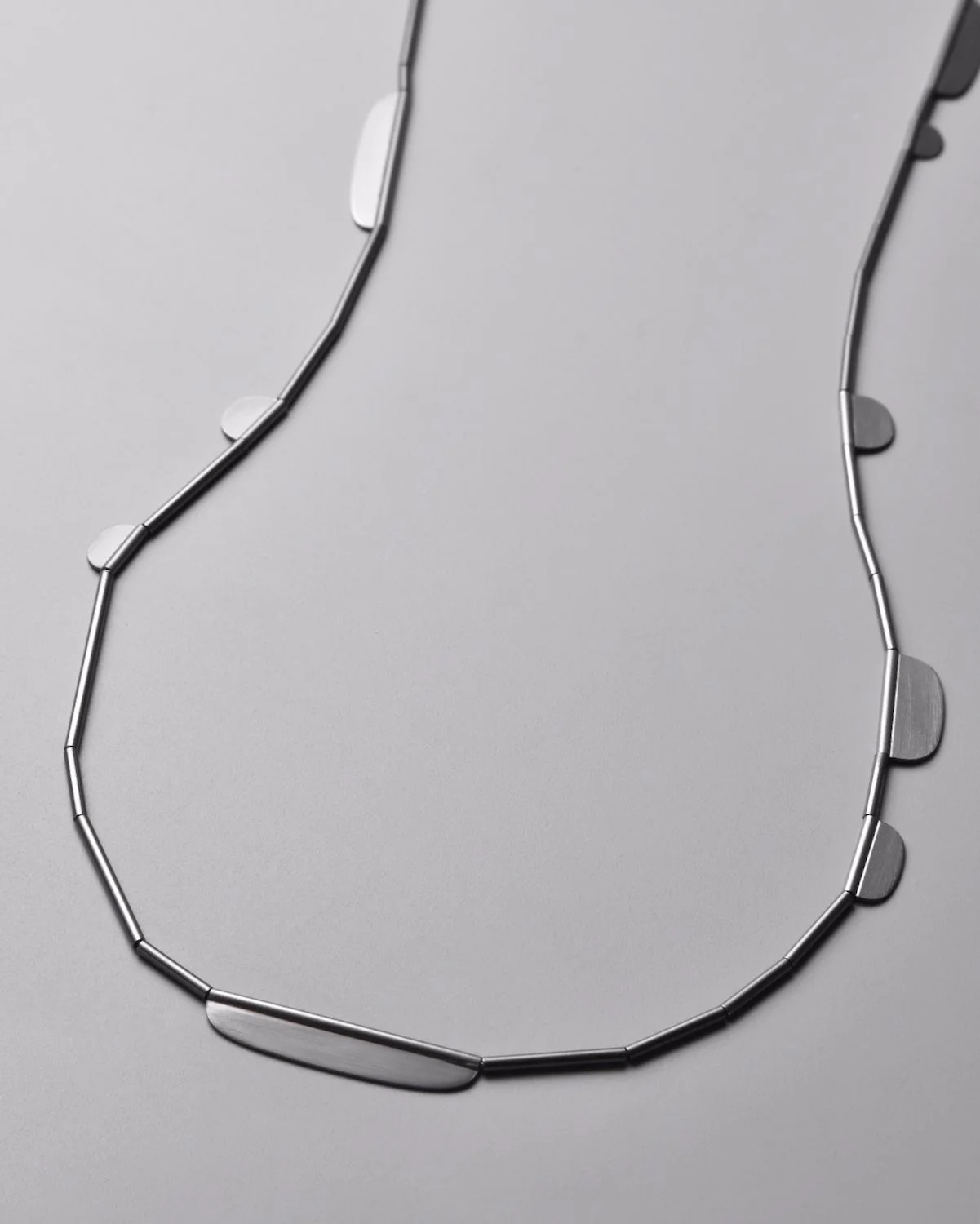 Finn Necklace in Oxidized Sterling Silver — close-up flat-lay detail of the dark oxidized silver chain on a grey background, showing the continuous loop