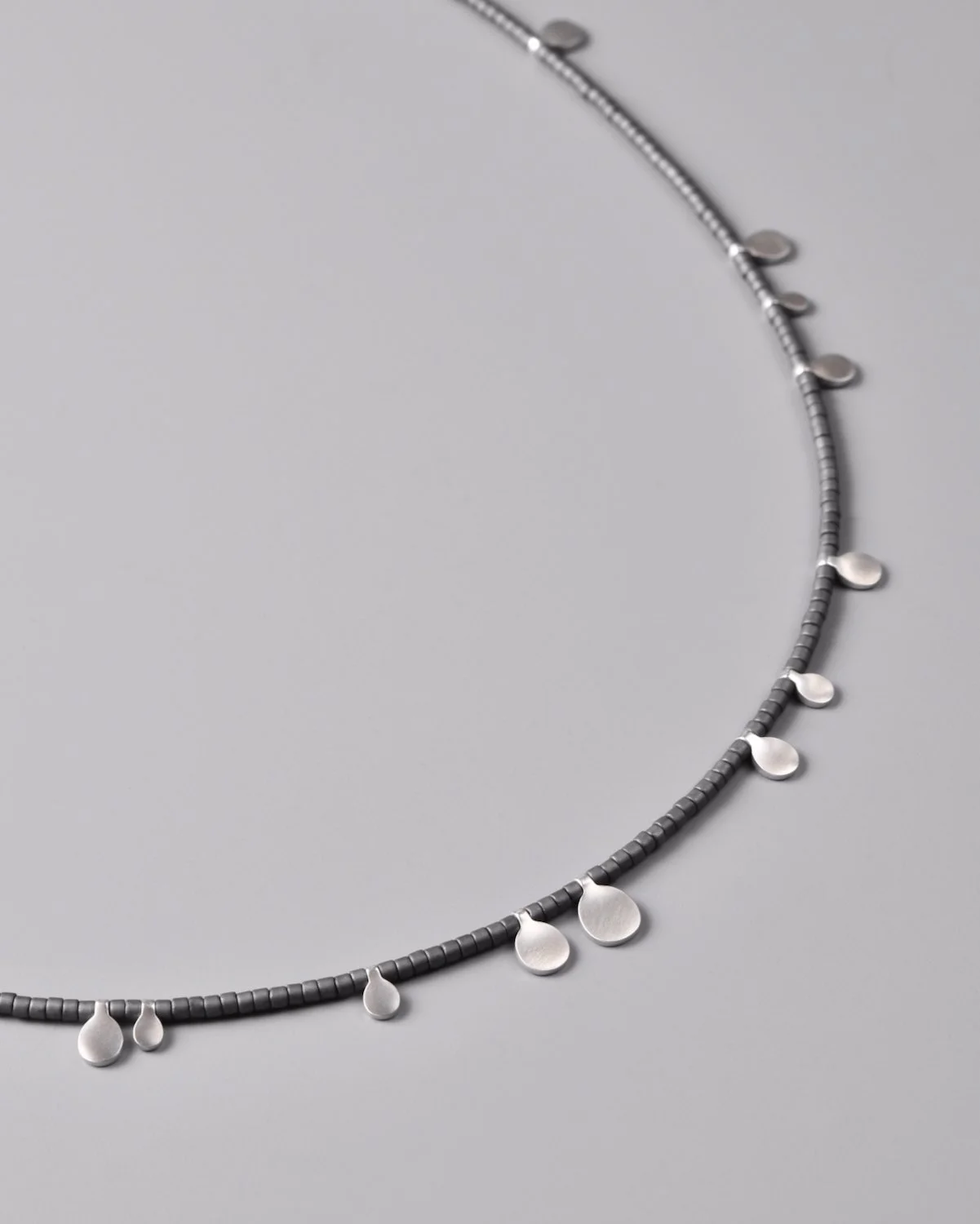 Diane Necklace — close-up flat-lay detail of charcoal grey glass beads and satin sterling silver droplets on a grey background