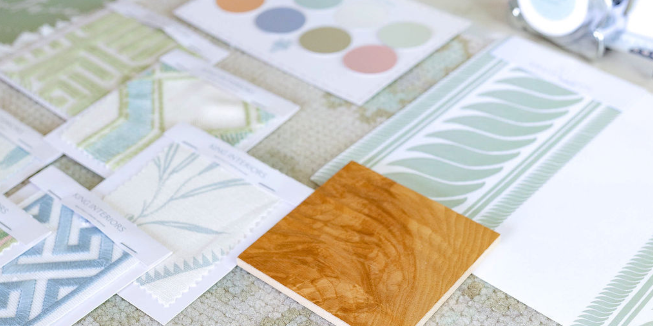 Samples of wallpaper and flooring materials in various patterns and colors, displayed on a flat surface for King Interiors Curated Virtual Design service.
