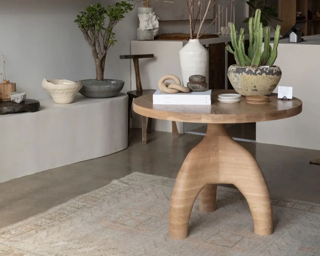 A wooden round table with curved carved legs, decorated with potted plants and decorative items, in a modern interior space.