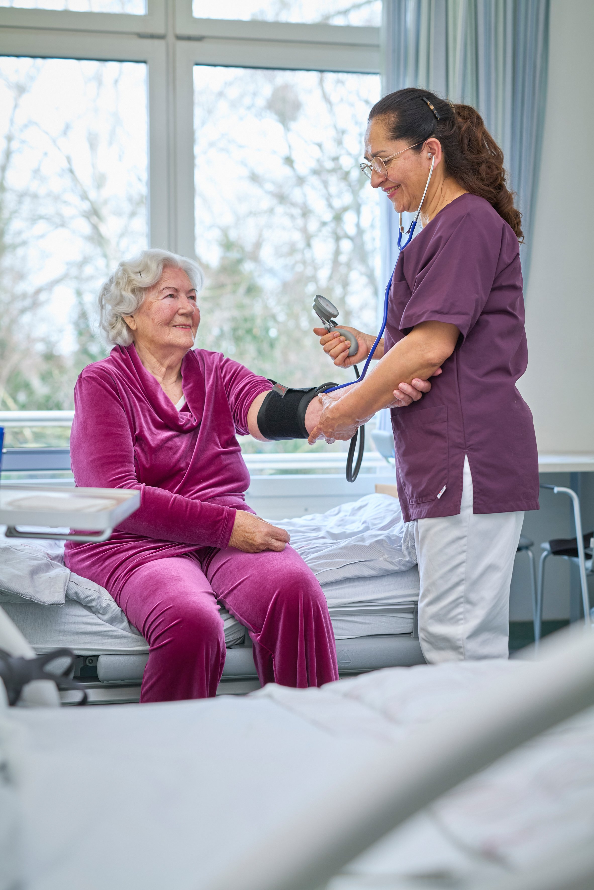 Eine Krankenschwester misst einer älteren Dame den Blutdruck im Krankenhaus