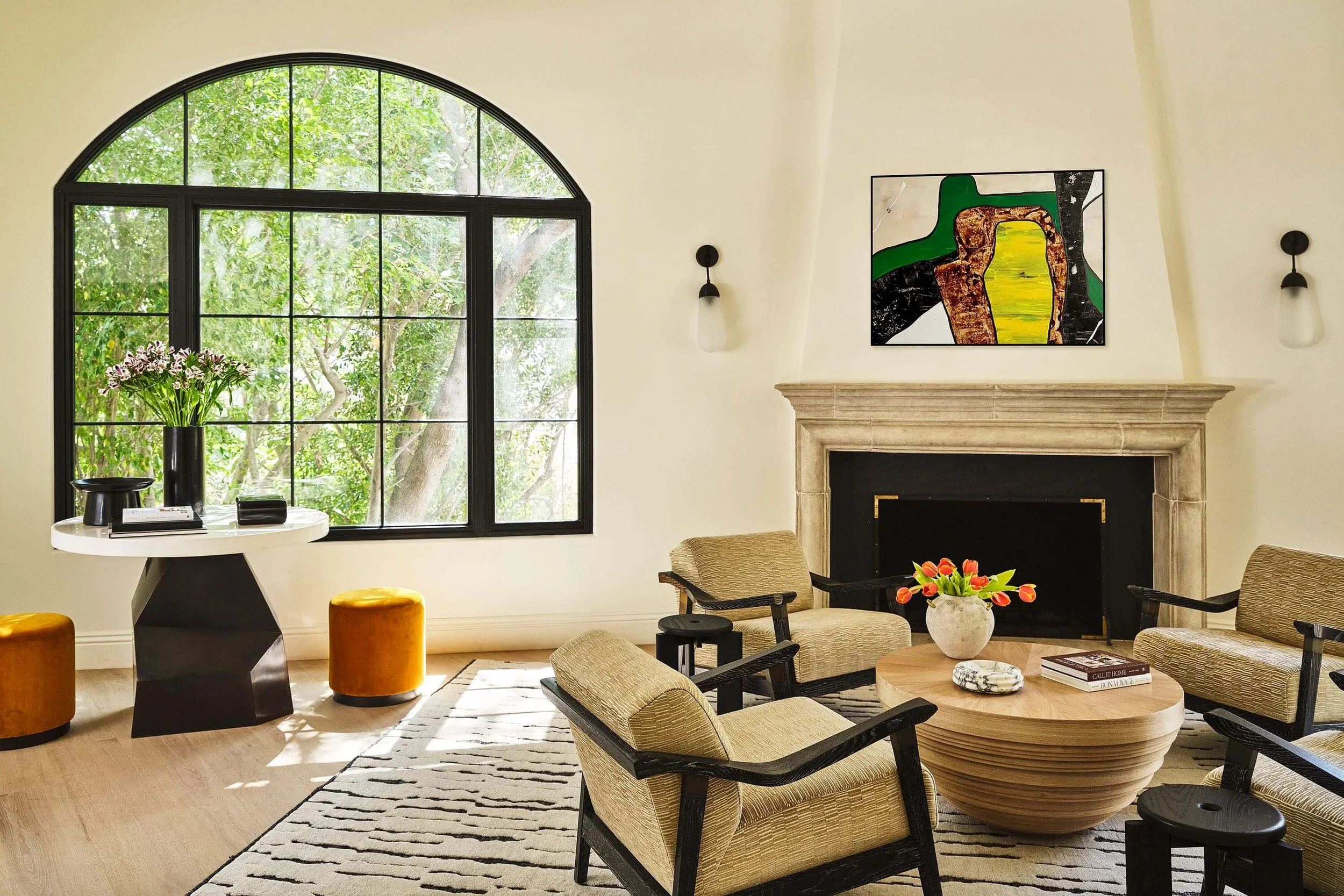 Hollywood Hills living room with arched steel window, stone fireplace, custom furnishings, and collected art.