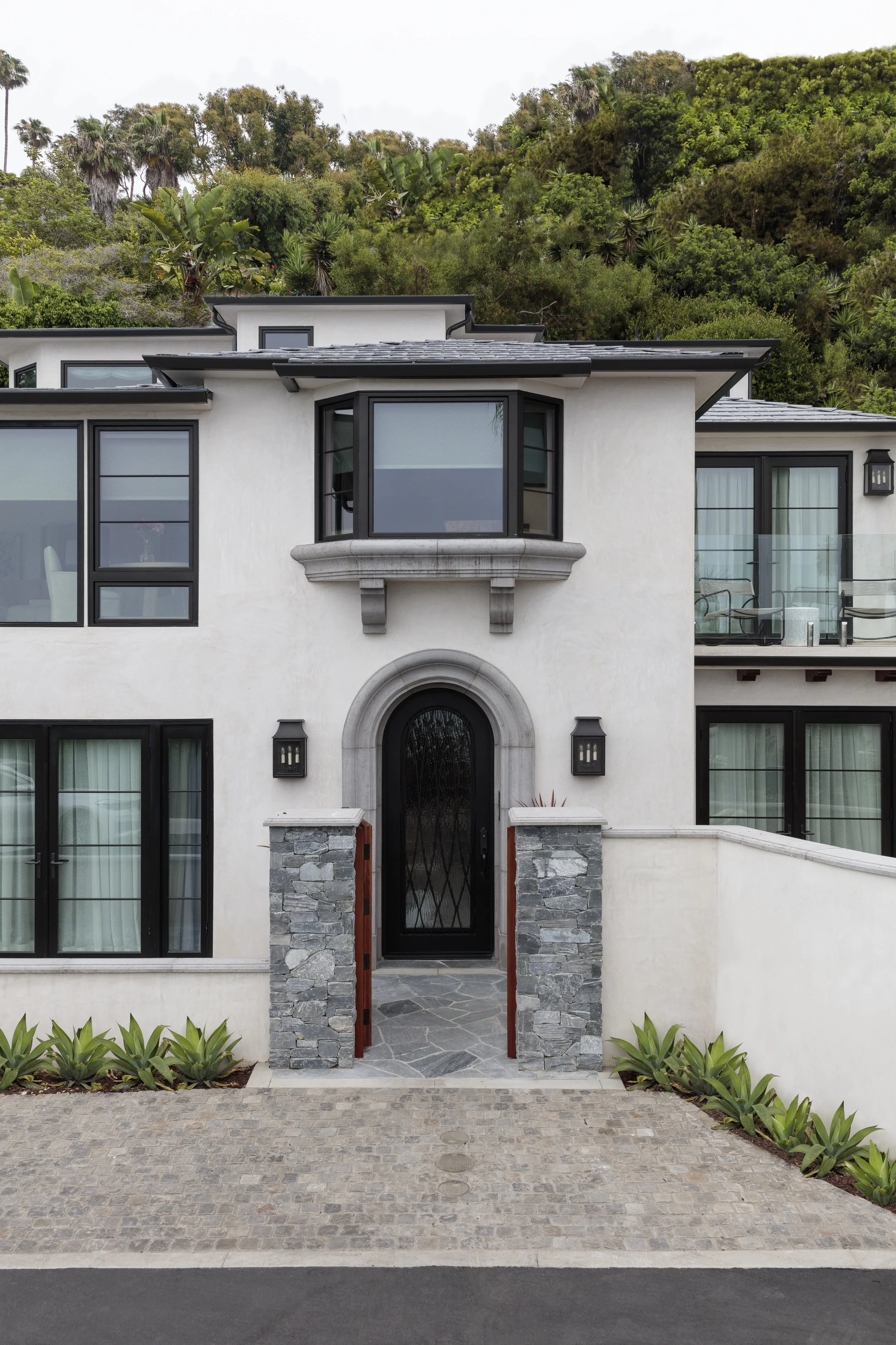 Stone archway with decorative black metal door, flanked by stone columns and lanterns, leading to a modern entrance.