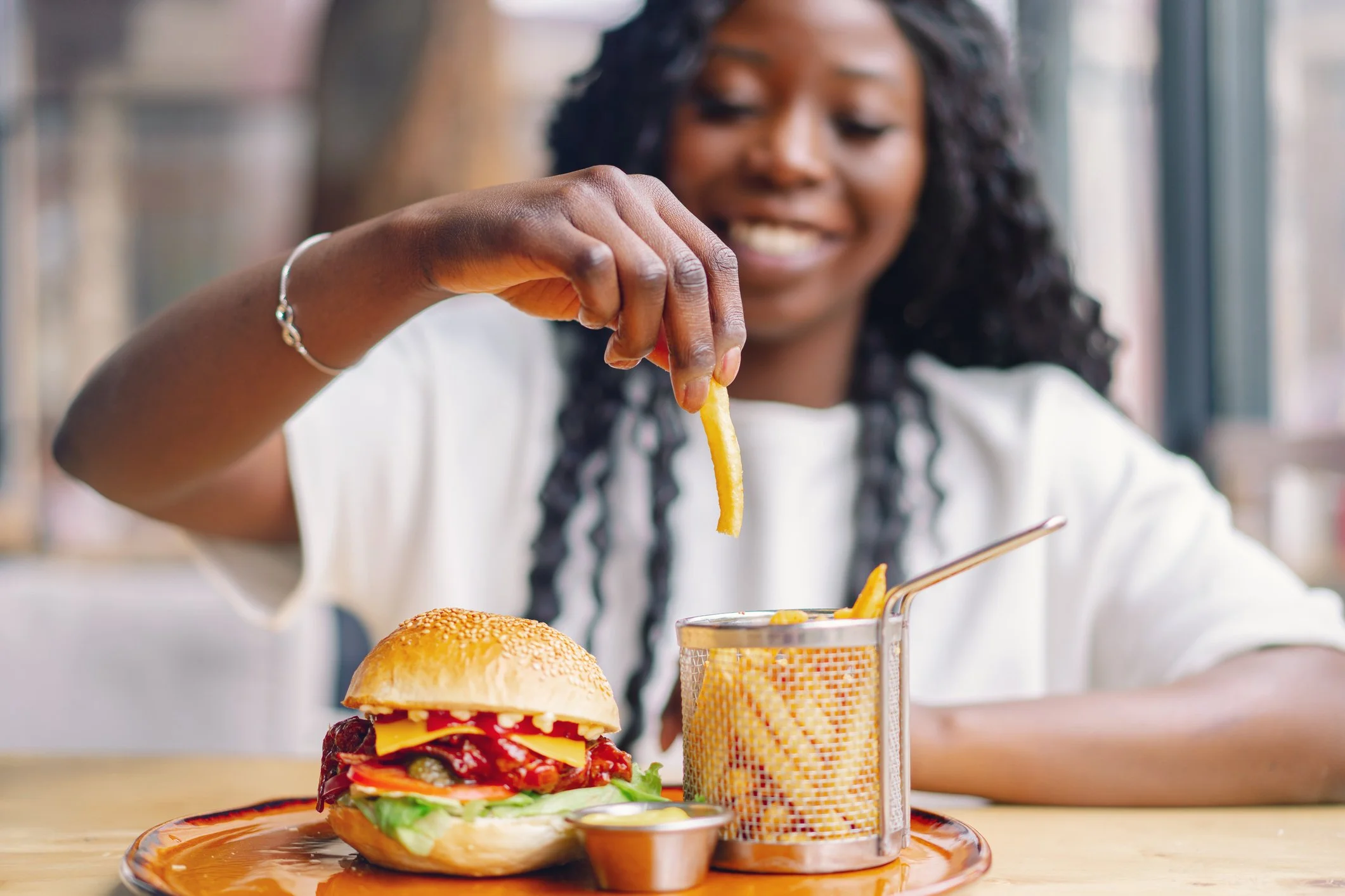 Woman sitting in front of meal of hamburger and fries picking up a fry
