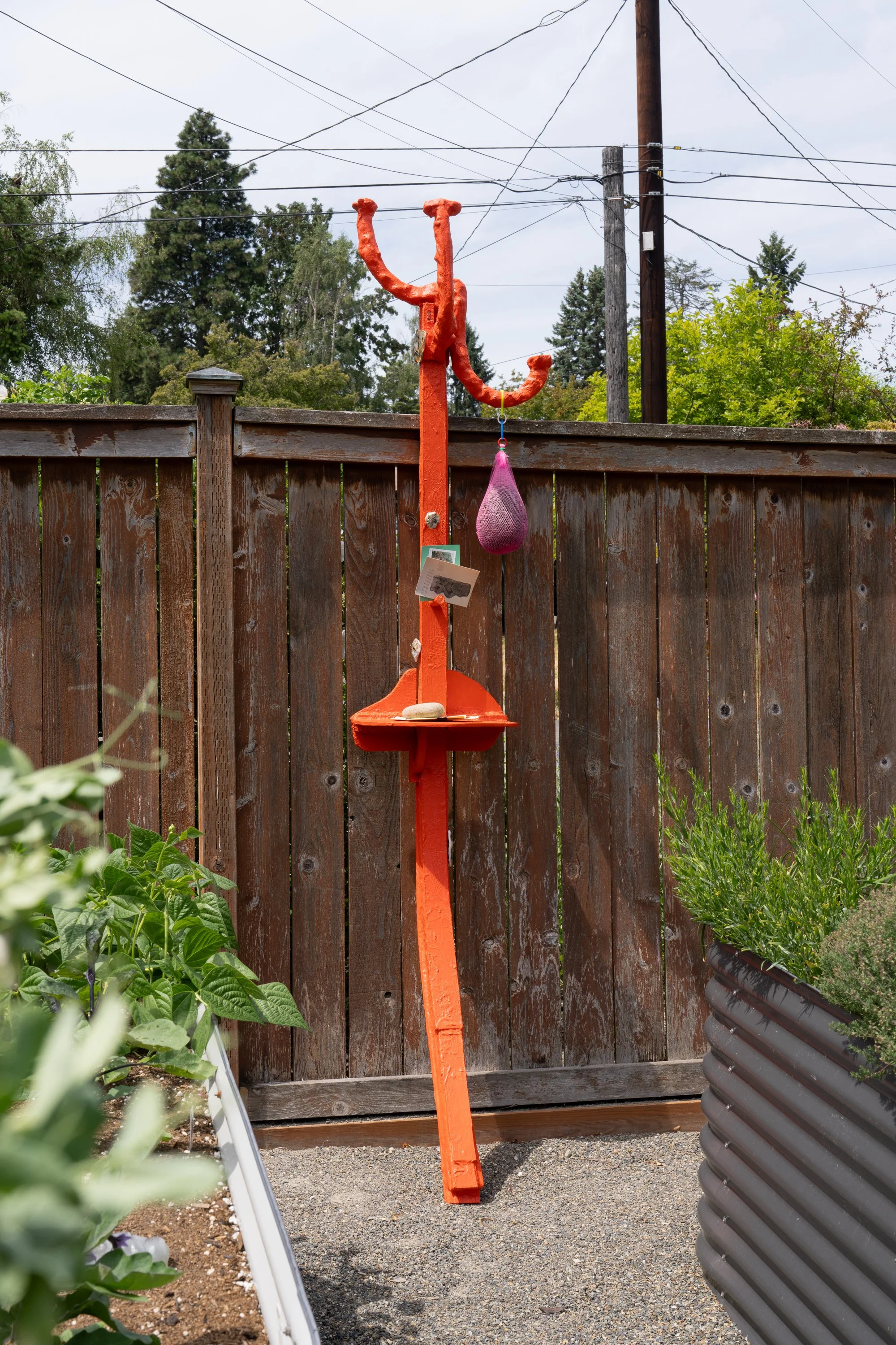 An orange sculpture leaning against a garden fence.