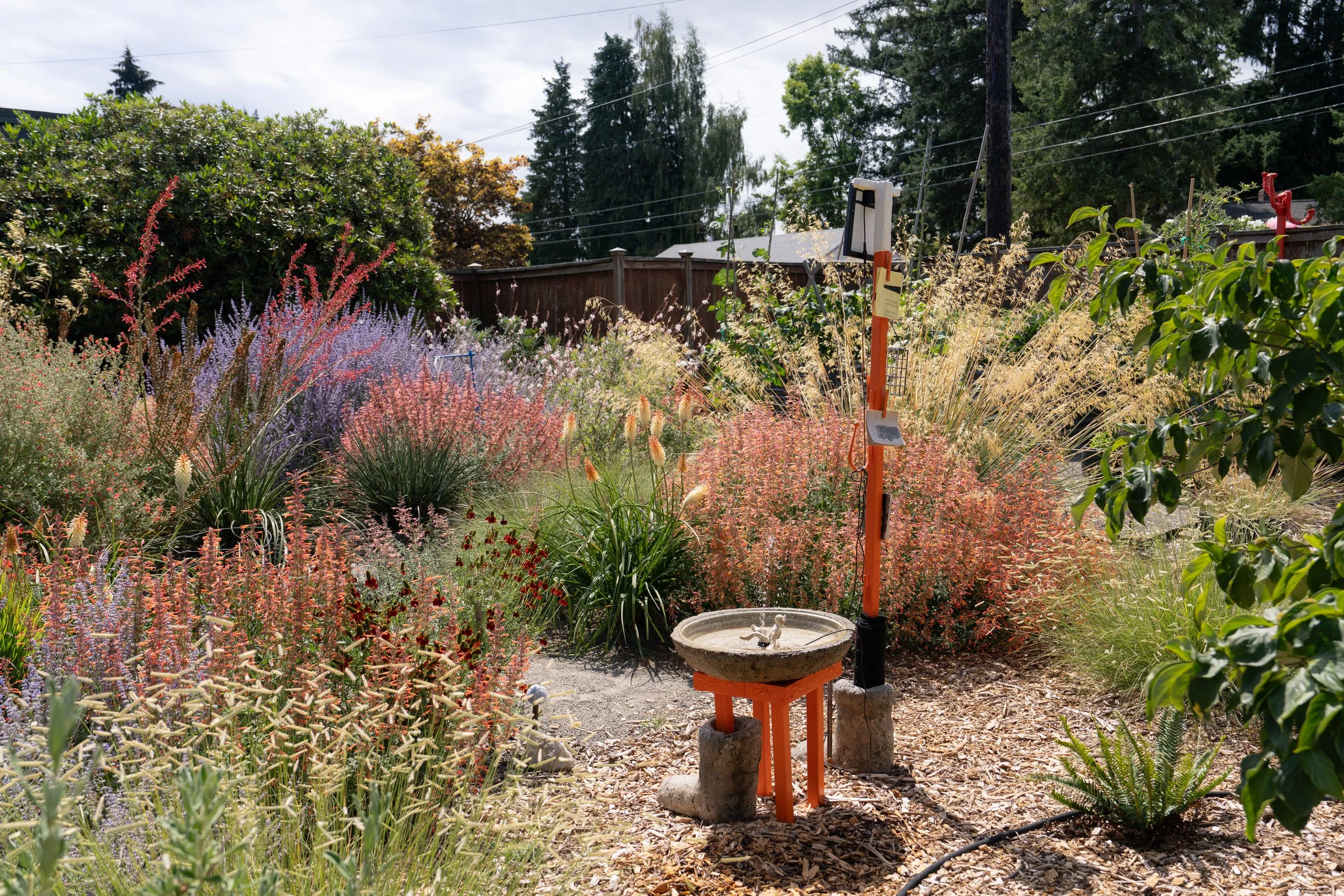 An orange sculpture with a fountain in a colorful garden.