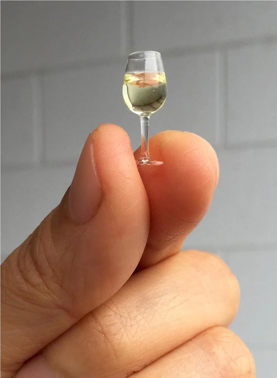 A hand holding a miniature wine glass.