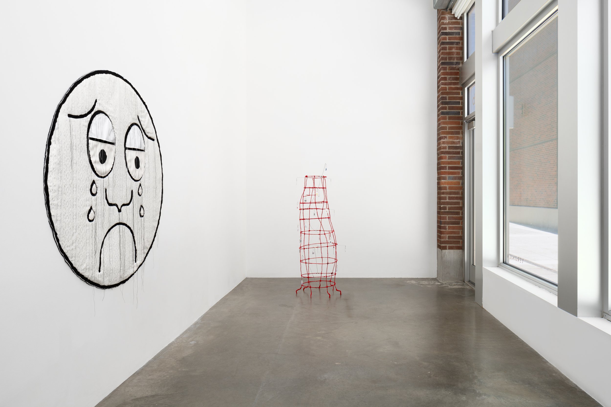 A crying face made of textile and a red sculpture in a gallery.