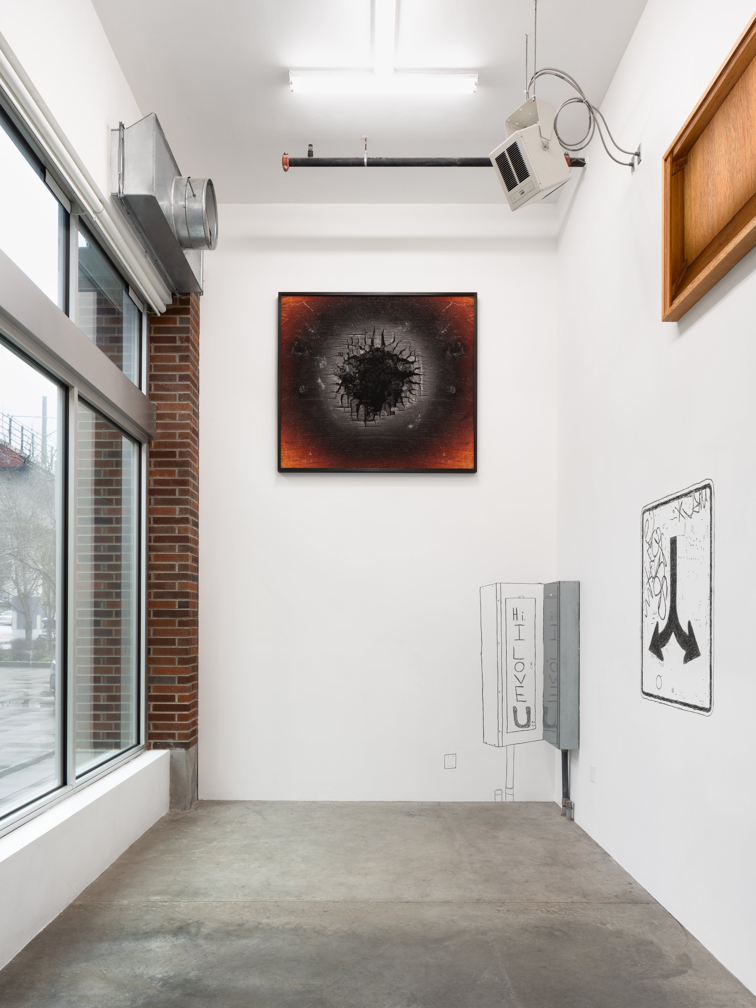 Large photographs depicting charred wood and interior of wood box high on walls and 2 charcoal drawings depuicting a traffic sign with arrows and the gallery panel box with text.