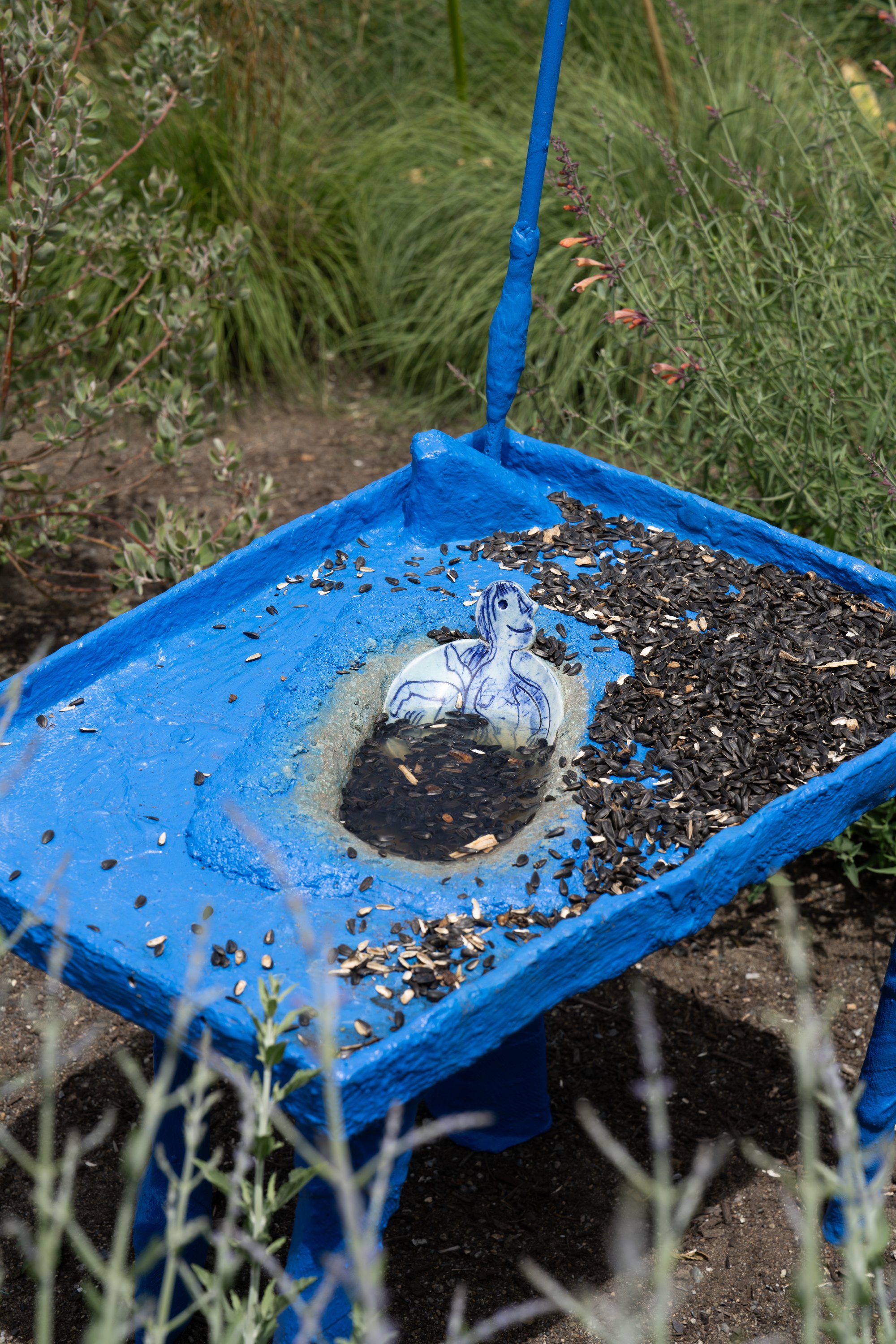 Sunflower seeds and a ceramic plate with a figure in a blue sculpture.