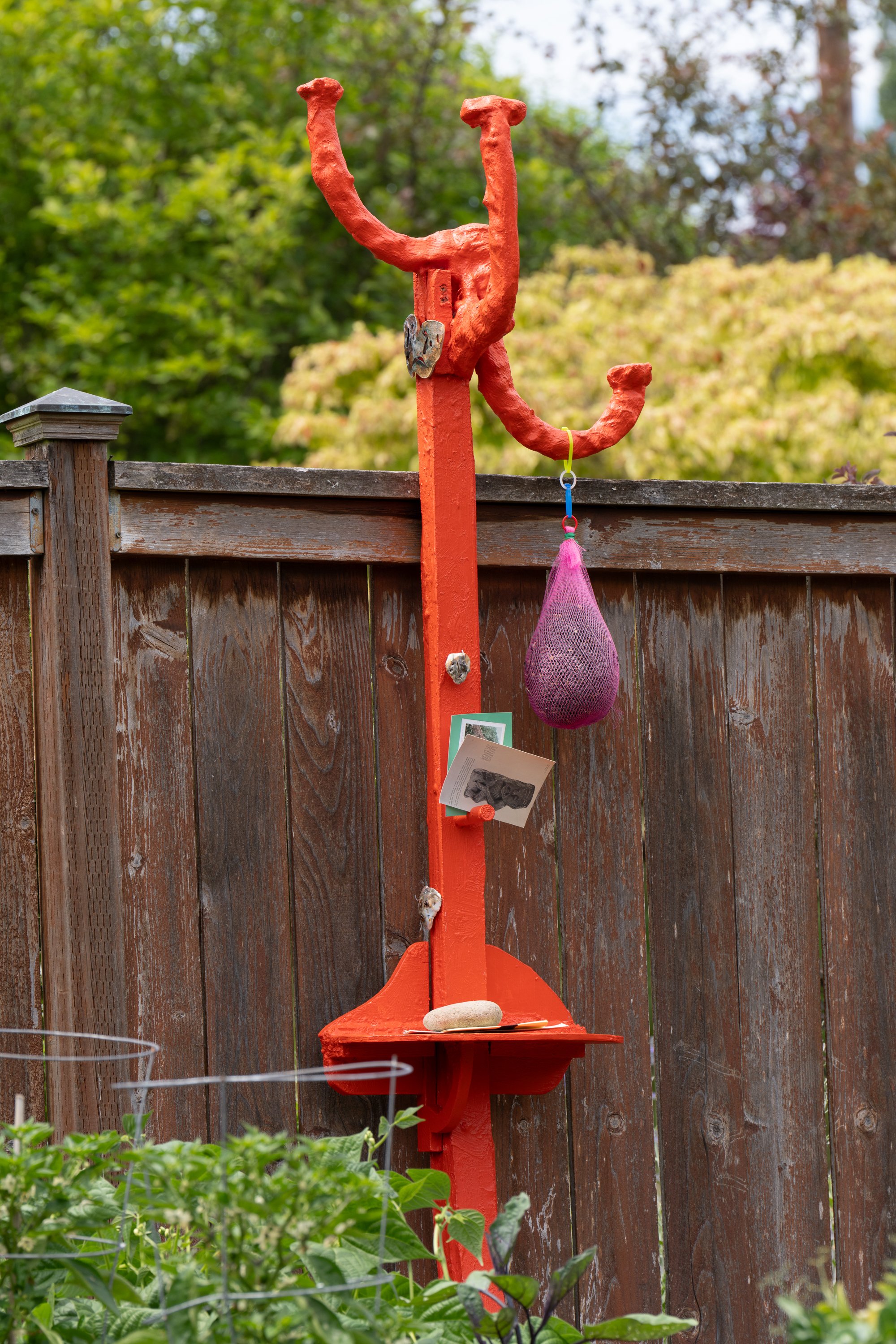 An orange sculpture leaning against a garden fence.