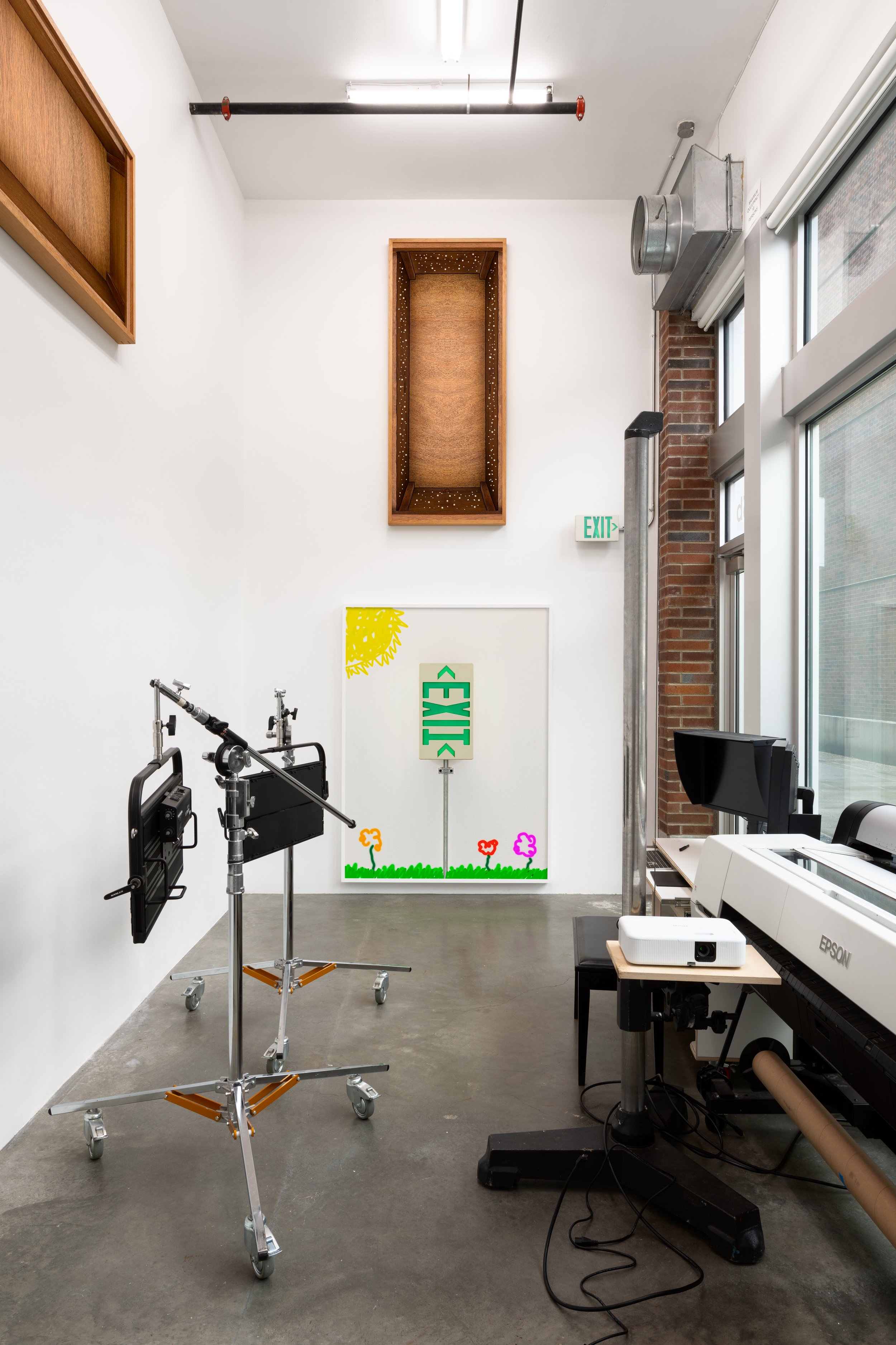 Gallery space with digital photo equip and photographs hung very high on the walls. One photo of the room's exit sign plus digital drawings is hung at "normal" height.