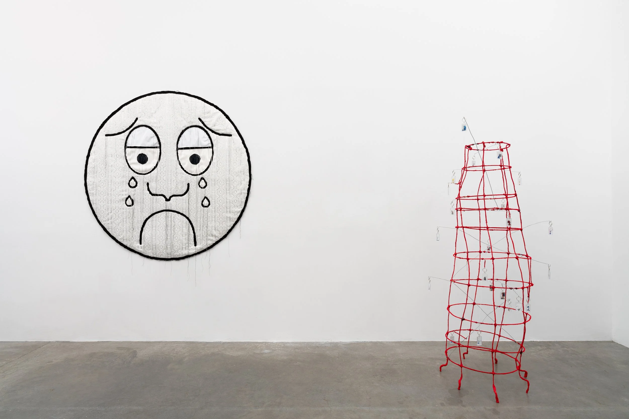 A crying face made of textile and a red sculpture in a gallery.