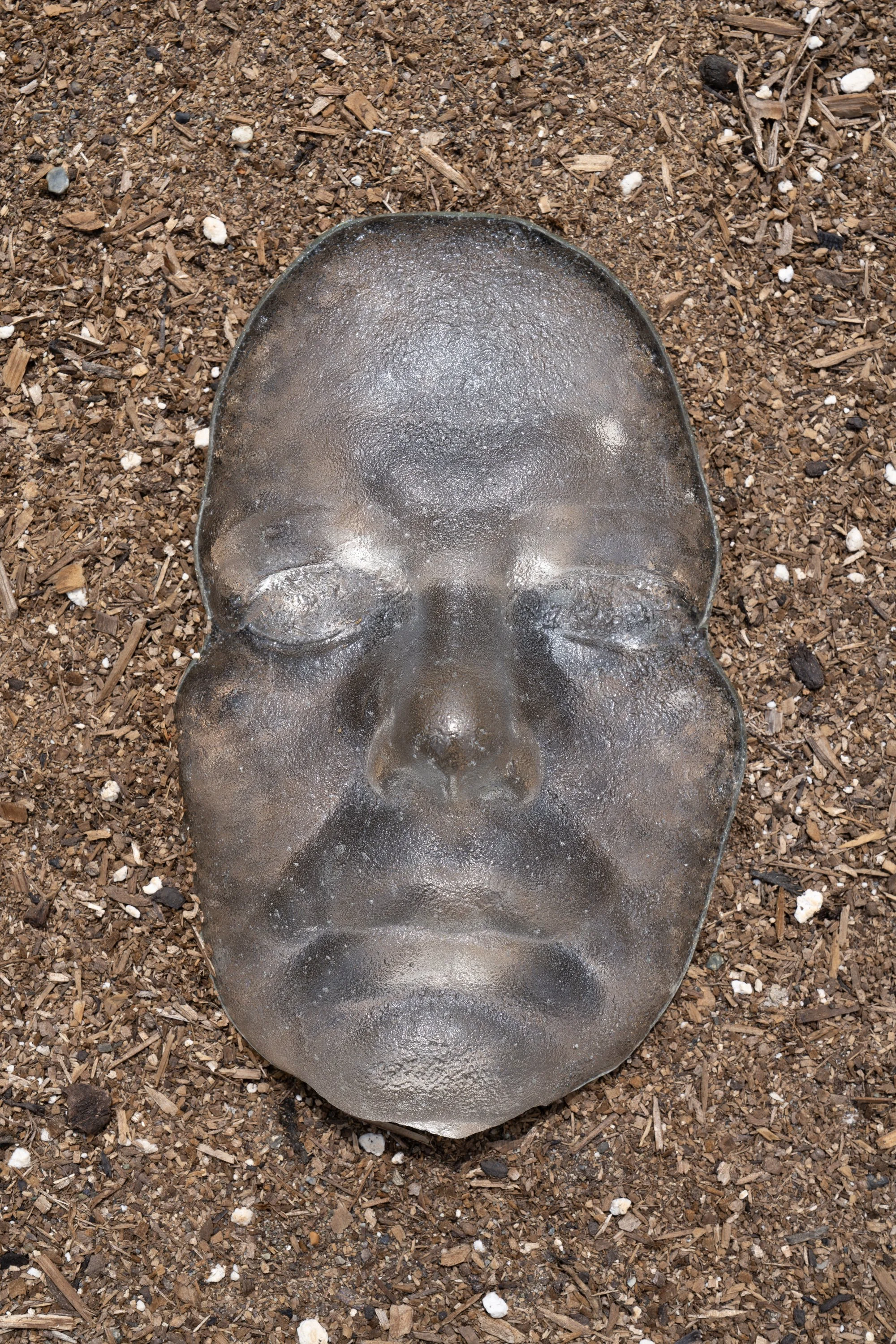 A glass face in a garden bed.