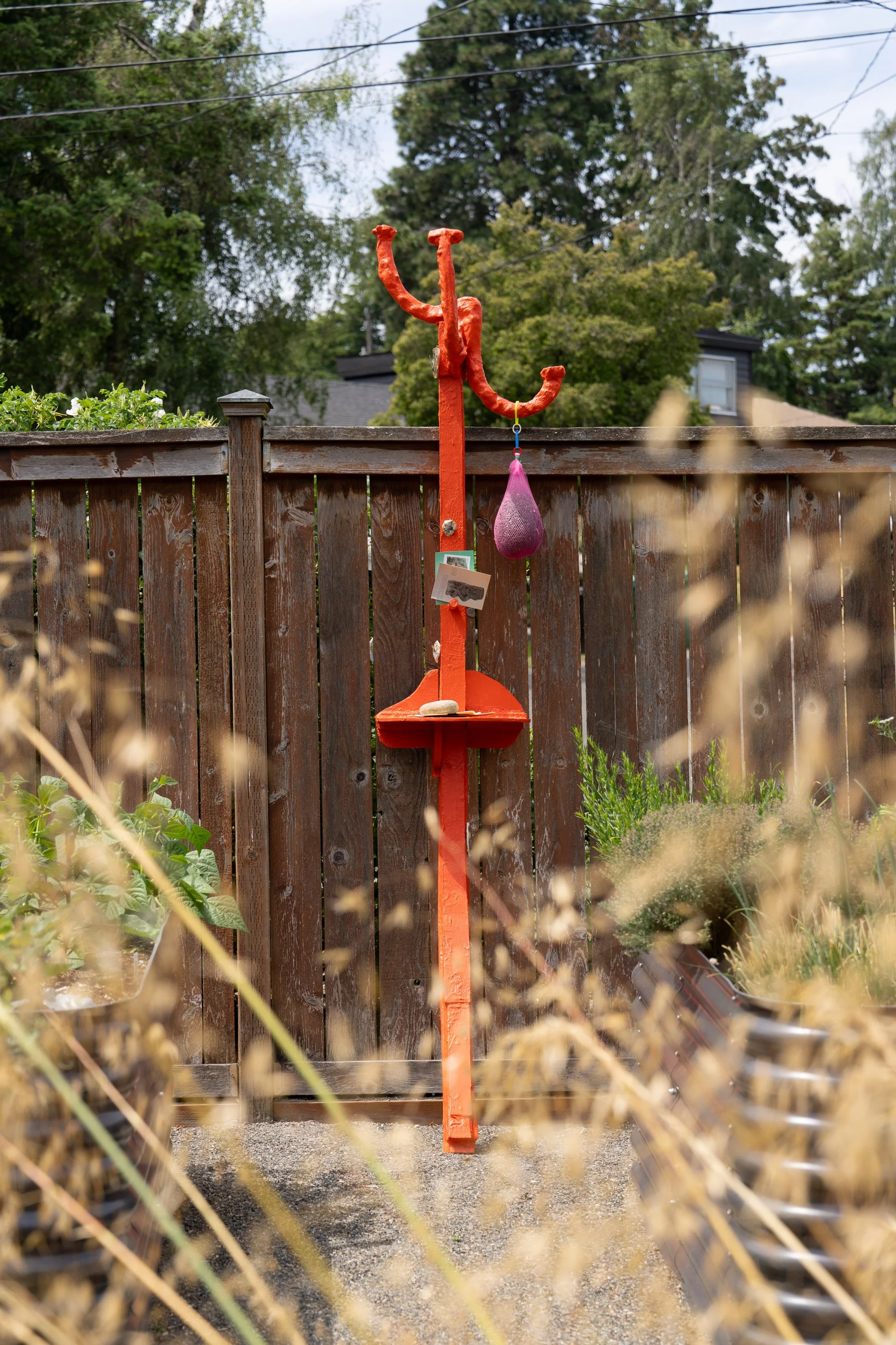 An orange sculpture leaning against a garden fence.
