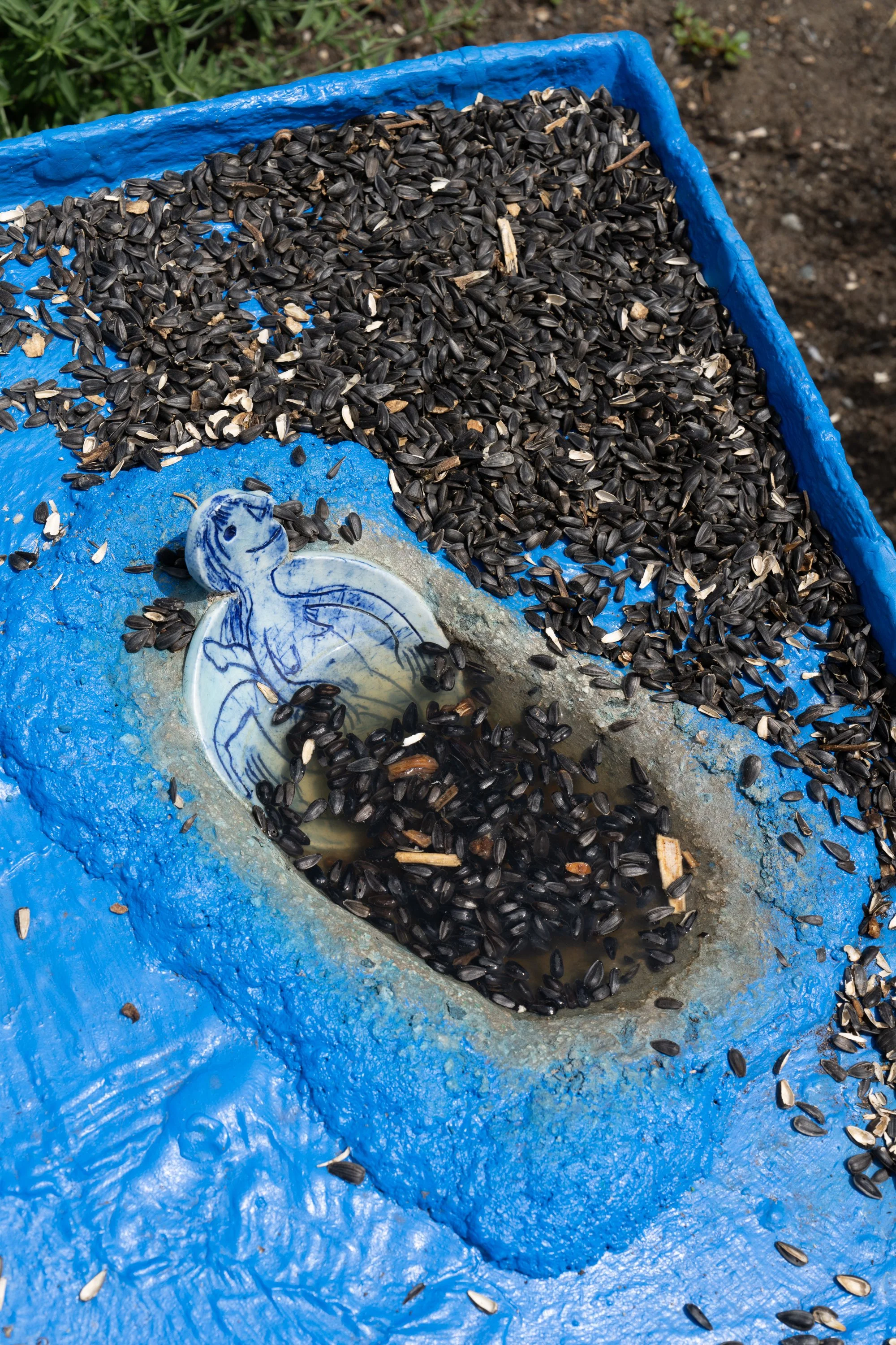 Sunflower seeds and a ceramic plate with a figure in a blue sculpture.