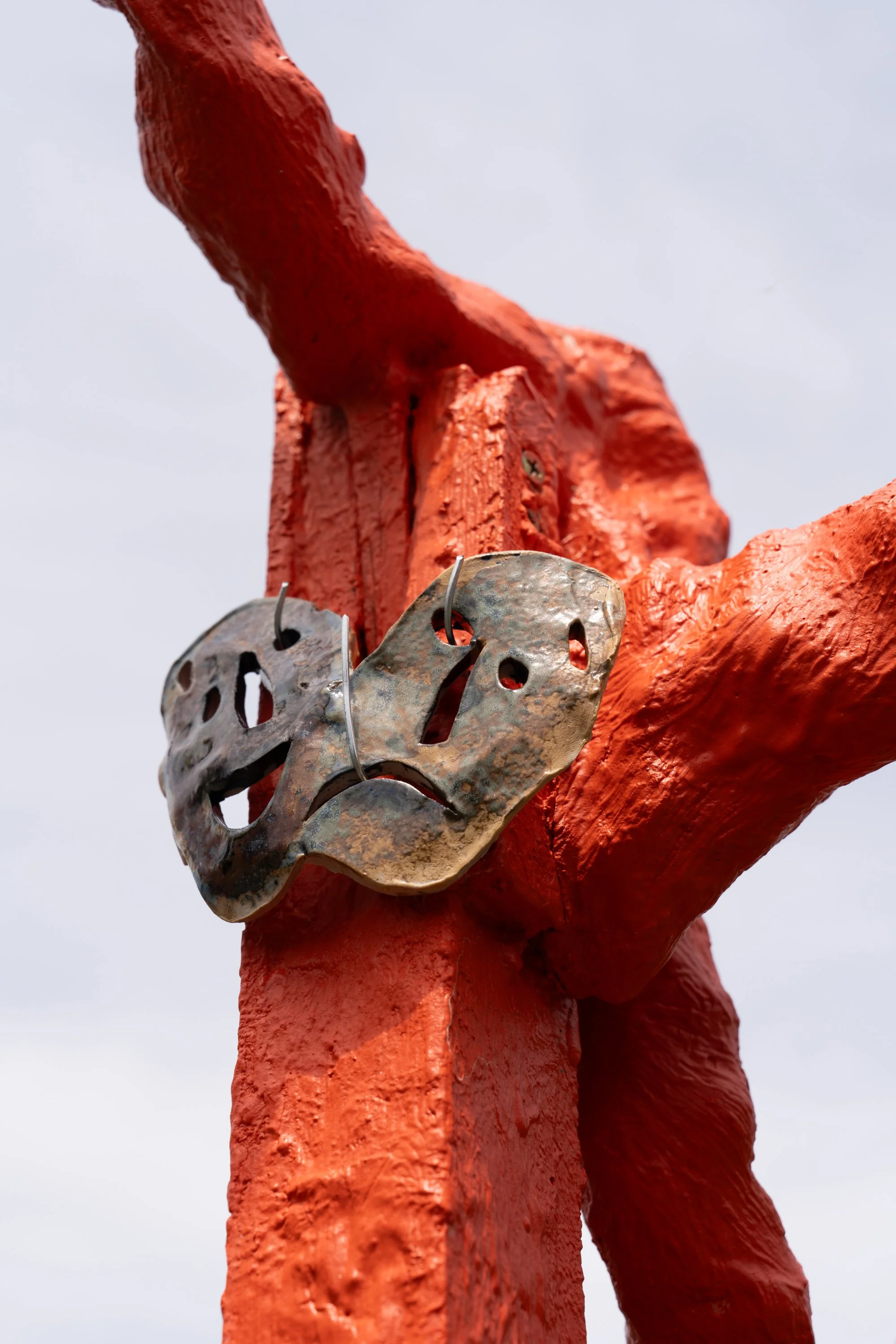 ceramic masks hung on an orange sculpture.