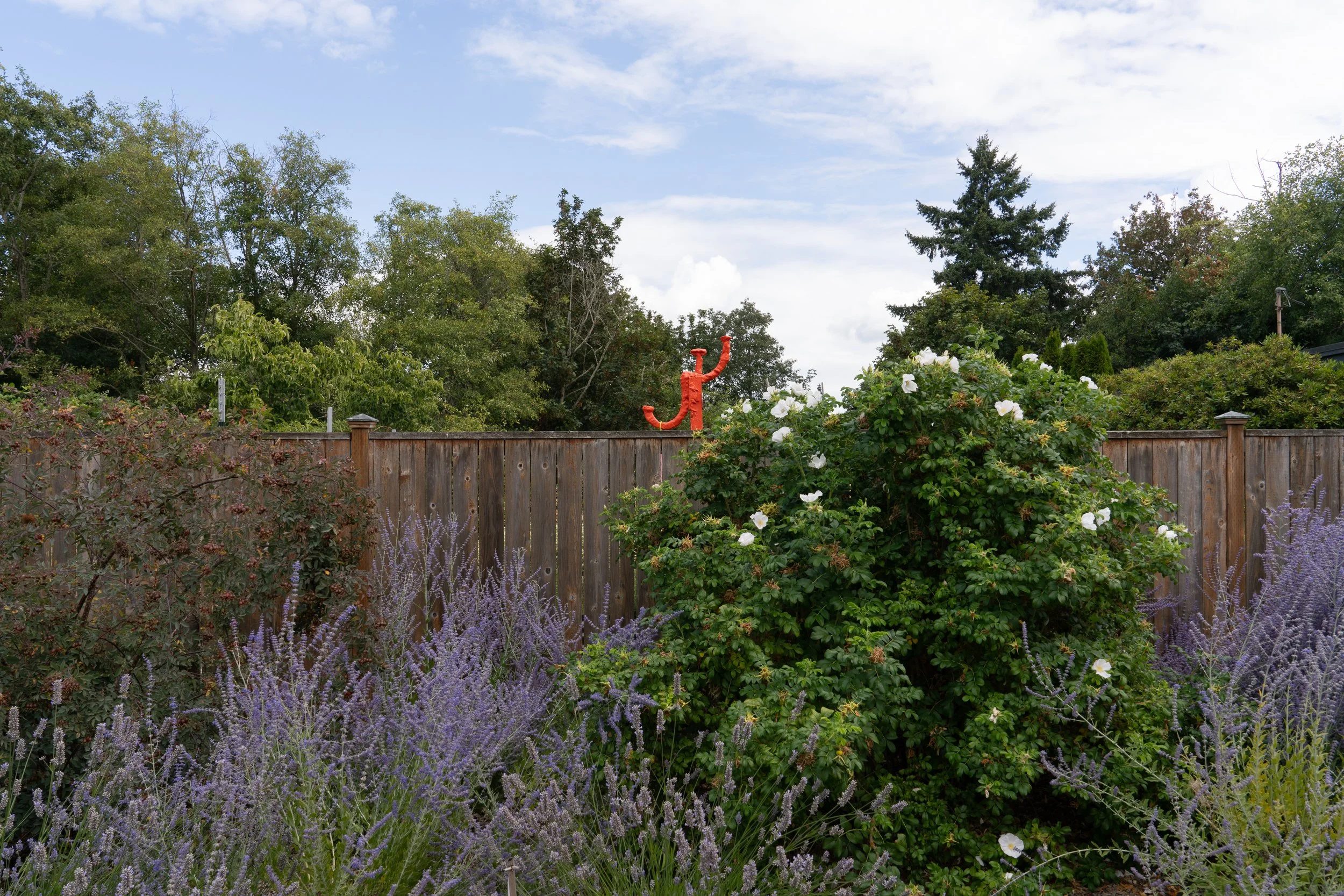 An orange sculpture peeking out of a garden fence.