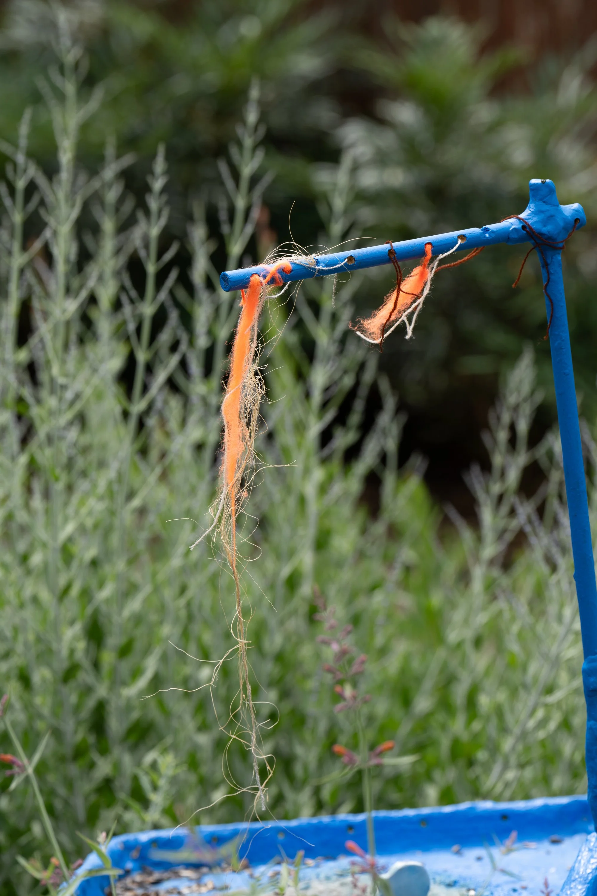 Orange twines ang red strings hung from a blue sculpture.