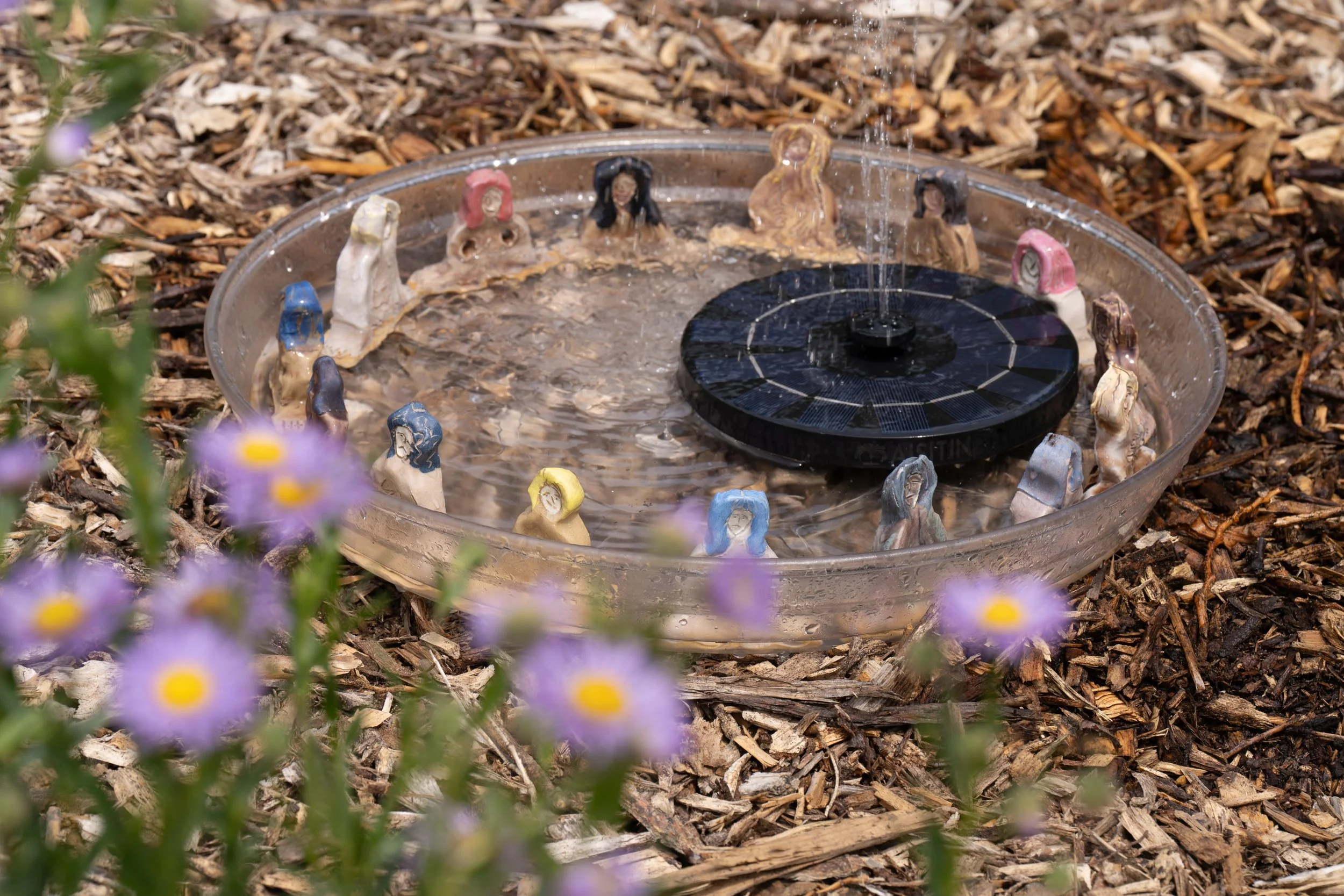 A water fountain in a plastic tray with ceramic bathing figures.