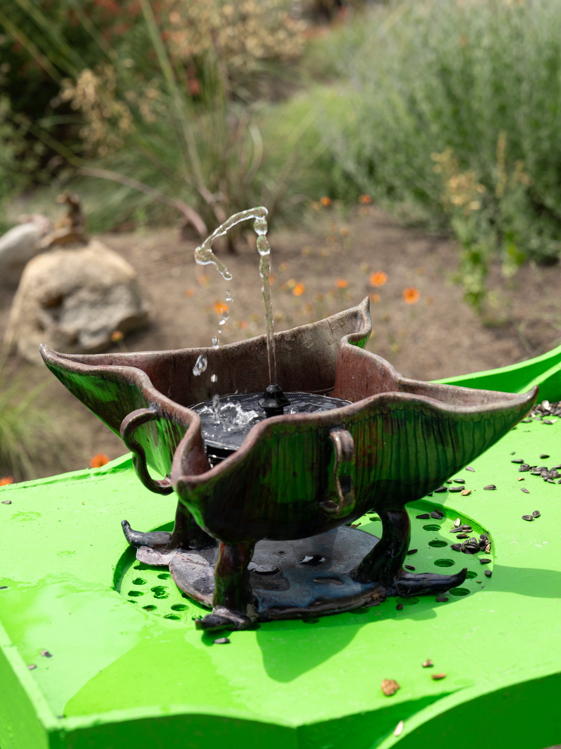 A water fountain in a ceramic vessle on green sculpture.