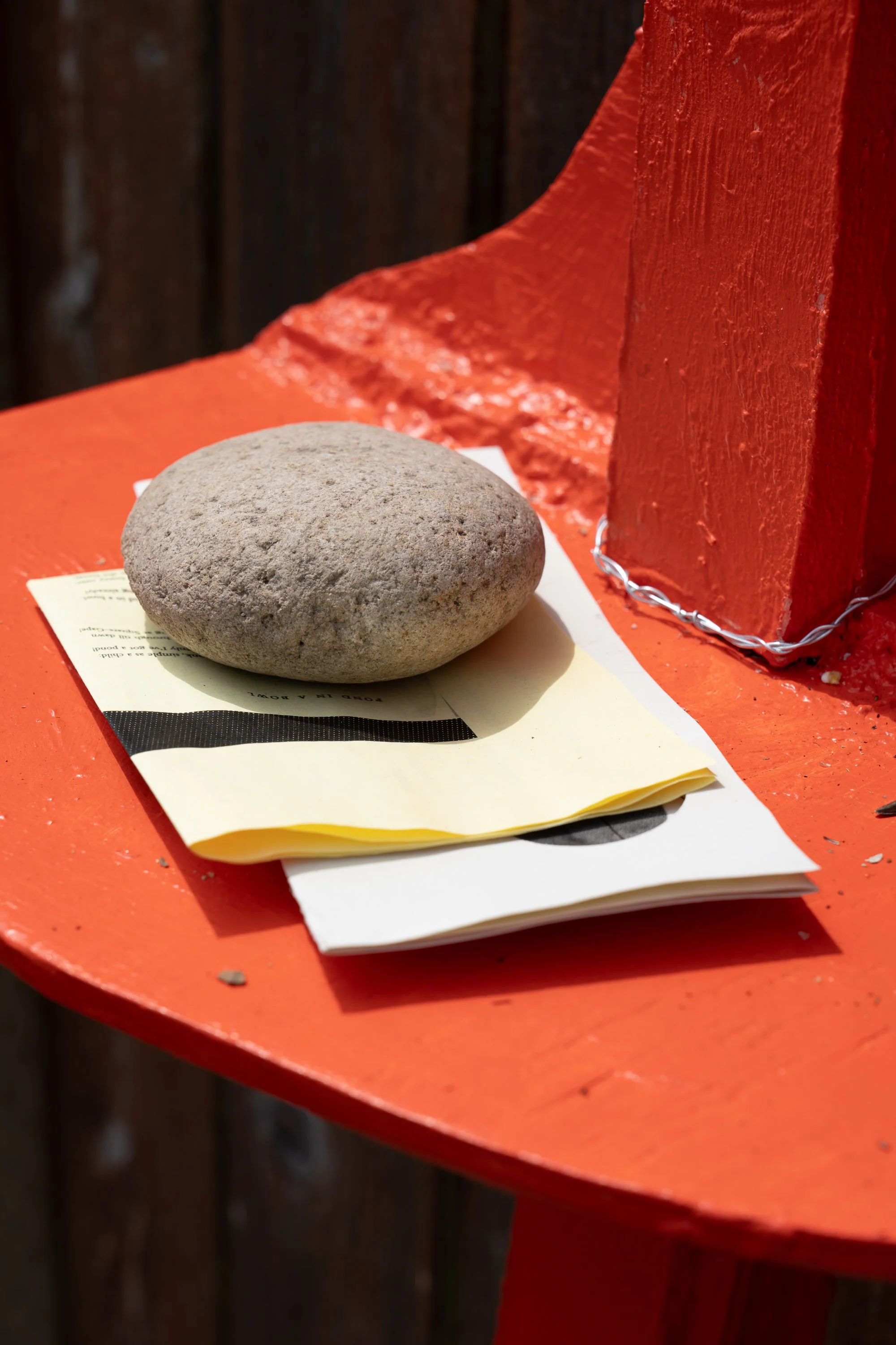Folded papers under a rock on an orange shelf.