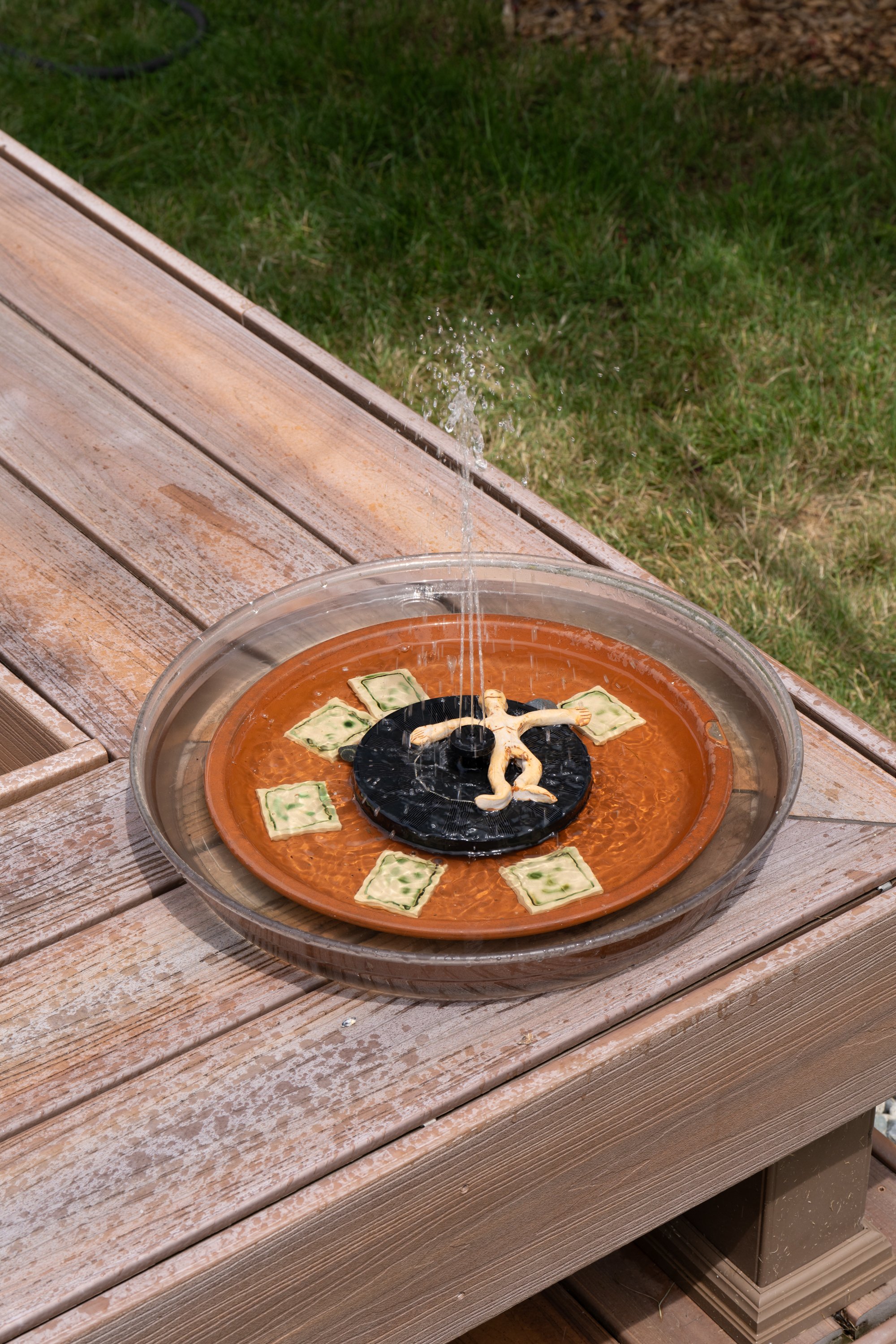 A water fountain in a tray with ceramic tiles and a ceramic figure.