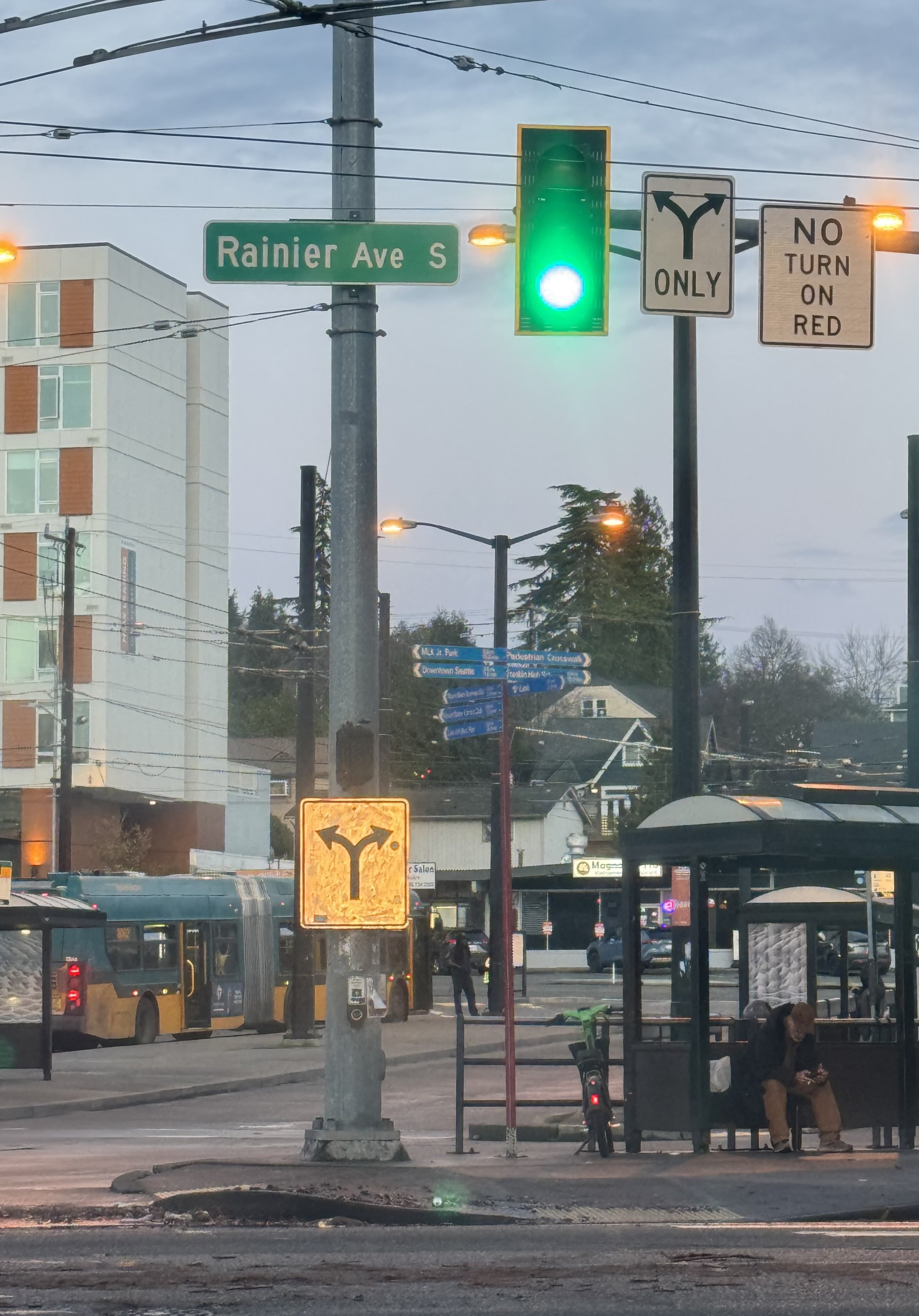 A road intersection on Rainier Ave S with a green light and 2 traffic signs that indicate left or right turn only.