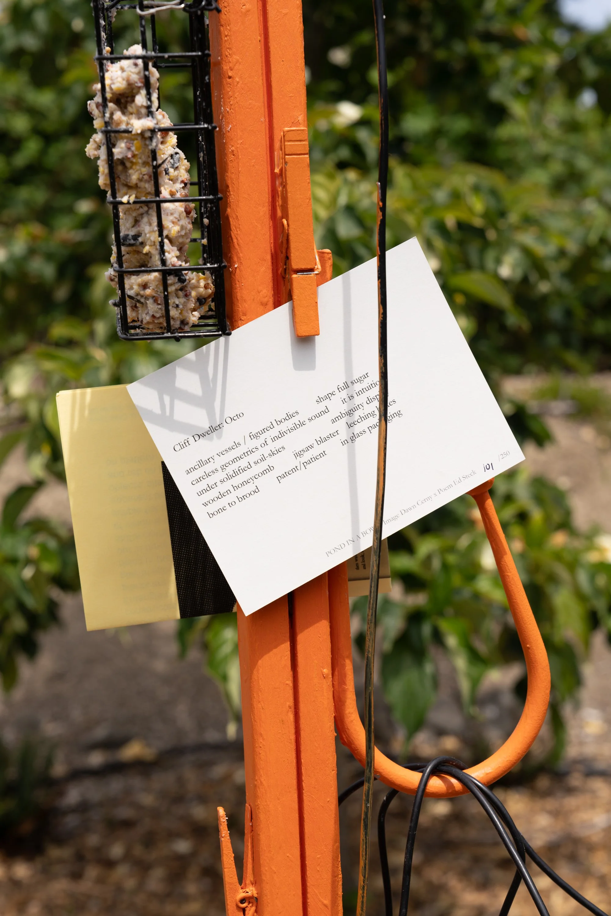 A poem on a postcard that is clipped onto an orange sculpture.
