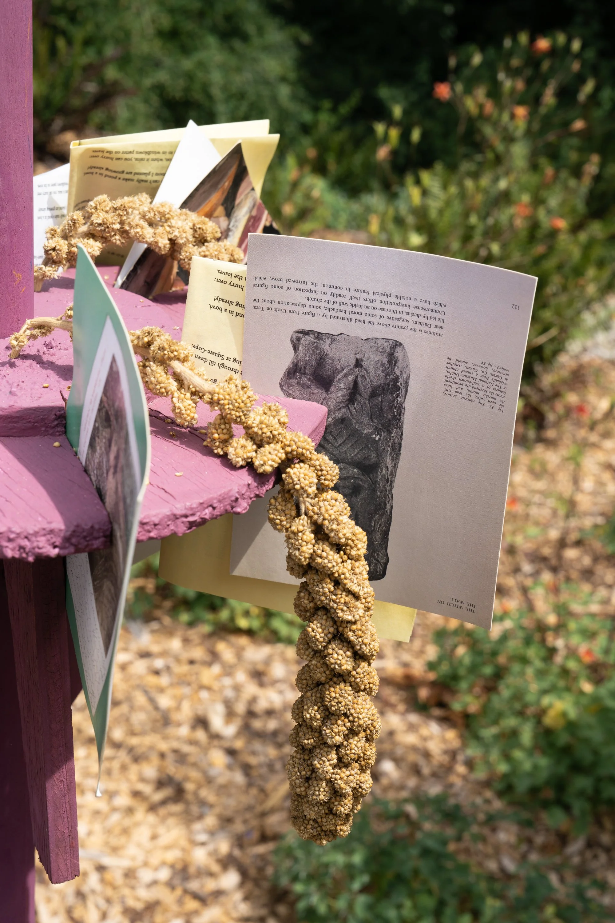Postcards, folded paper with texts, and bird feed on a pink sculpture.