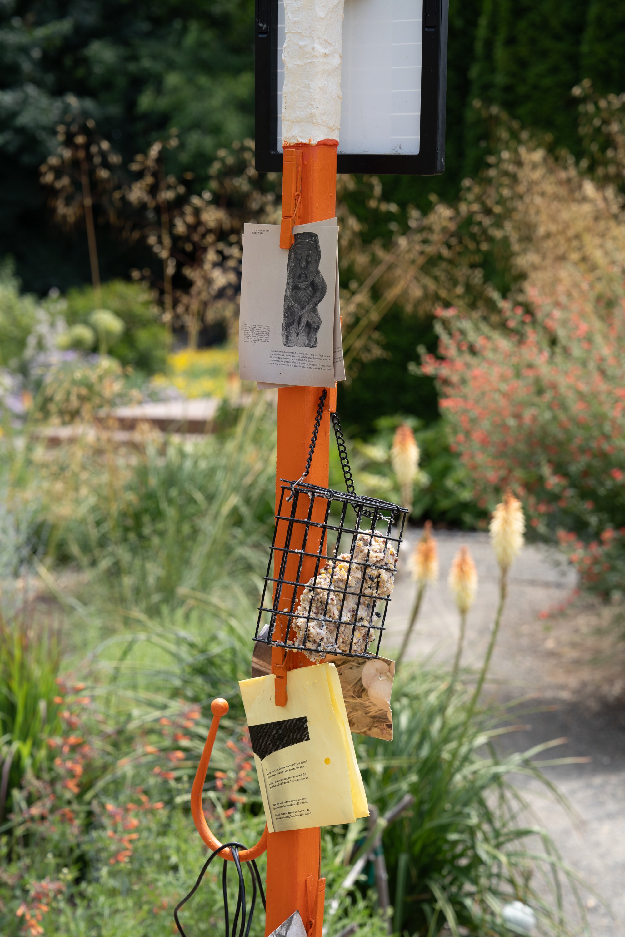 Postcards, folded papers, and suet bird feed hung from an orange sculpture.