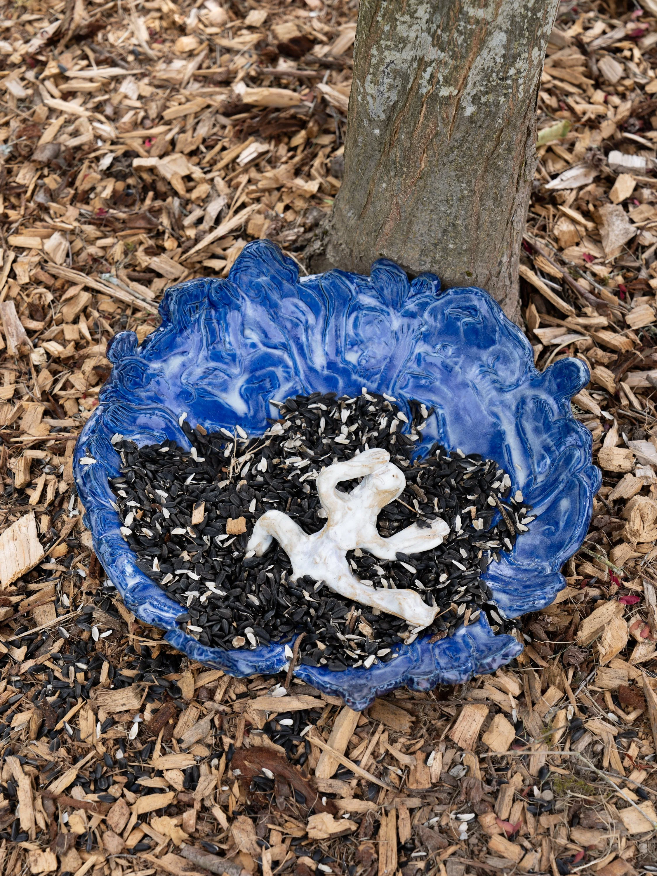 A blue ceramic bowl with sunflower seeds and a ceramic figure.