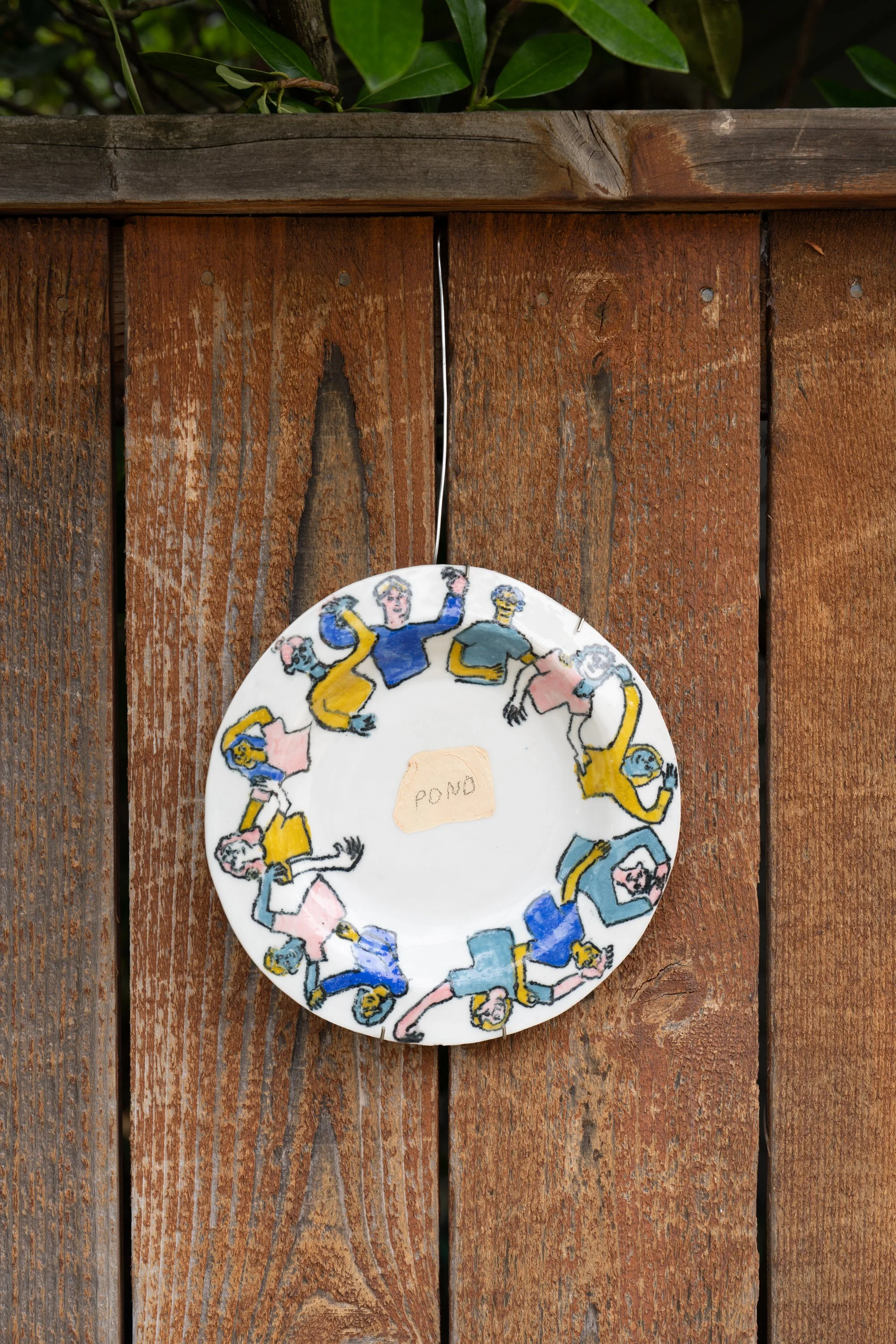 A ceramic place with the work "pond" hung on a wooden gate.