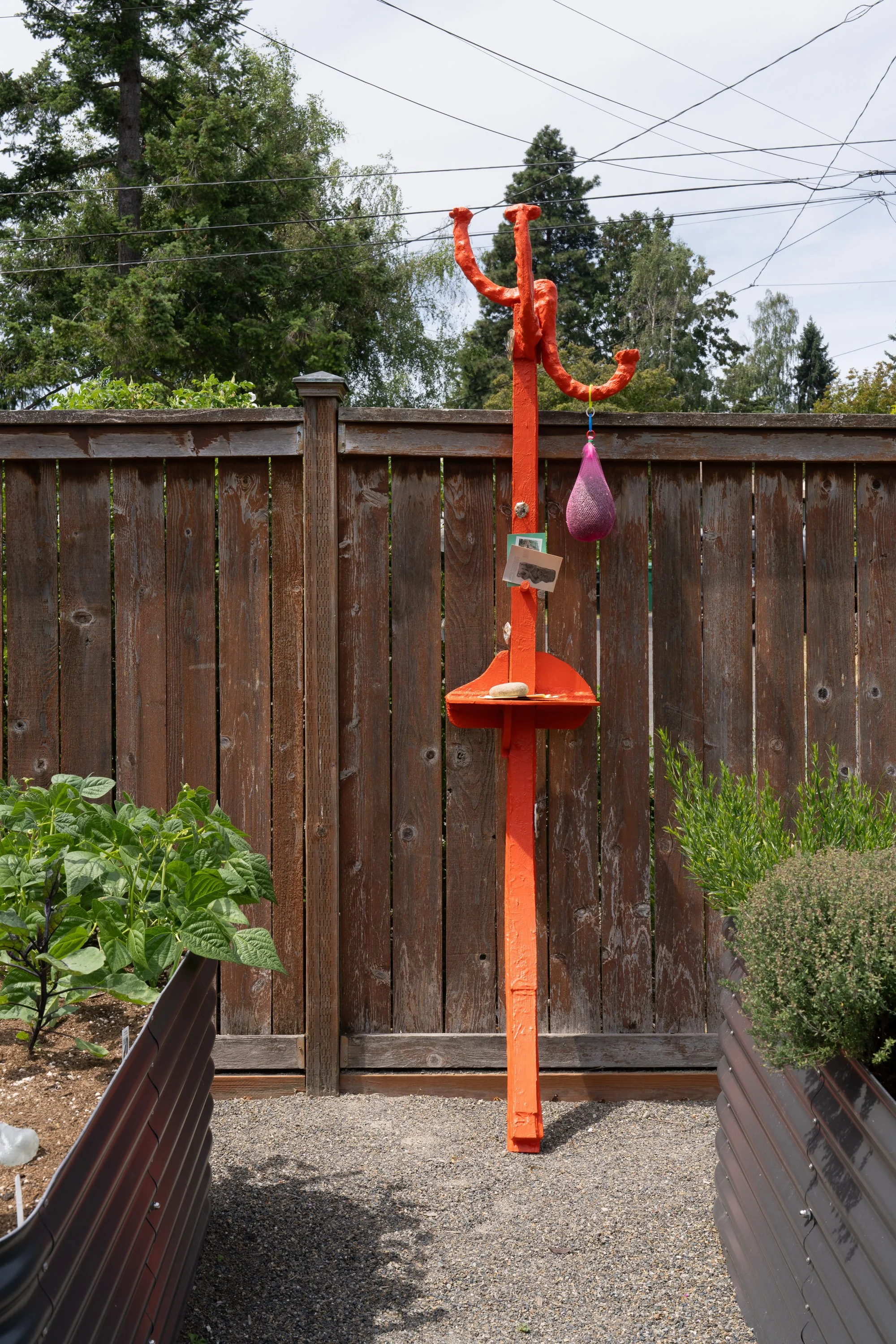 An orange sculpture leaning against a garden fence.