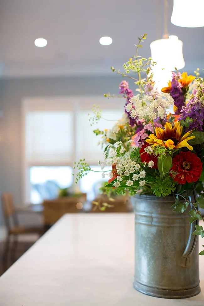 Elegance is in the eye of the beholder. A vintage watering can provided a lovely texture for the flowers arranged by August Lily Florist. (Sometimes we need professional assistance with home hugs!) Image: Wanda S. Horton Interior Design Photographer: Whitney Gray