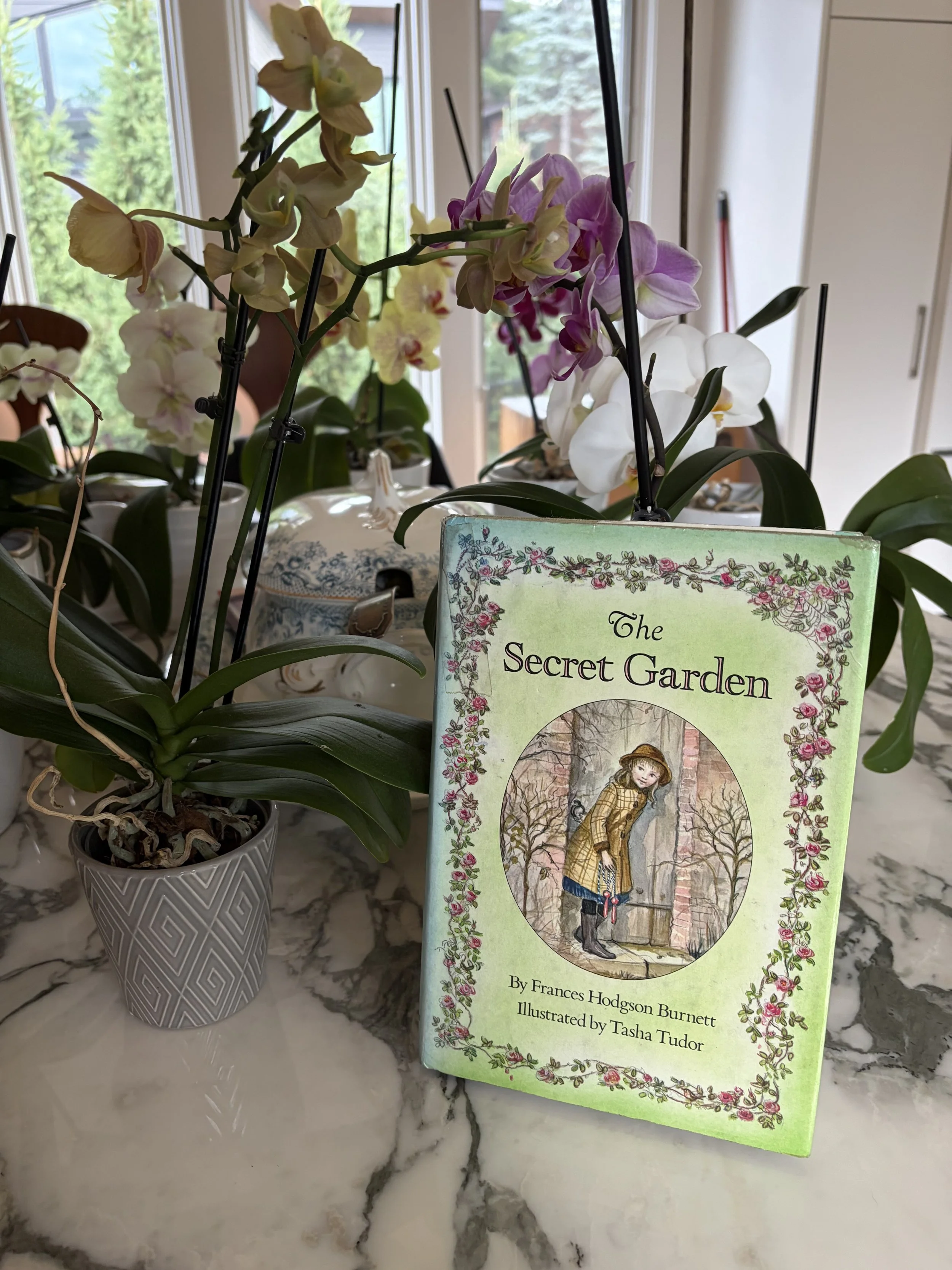 The book, Secret Garden, on a marble table with flowering orchids.