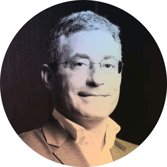 A man with glasses, short gray hair, wearing a suit jacket and light-colored shirt, smiling against a dark background.