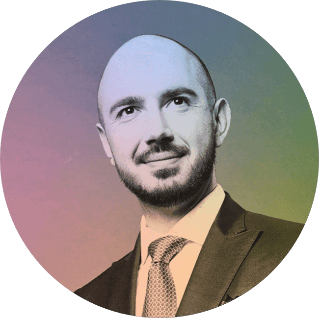 A man in a suit with a tie, smiling, with a gradient background.