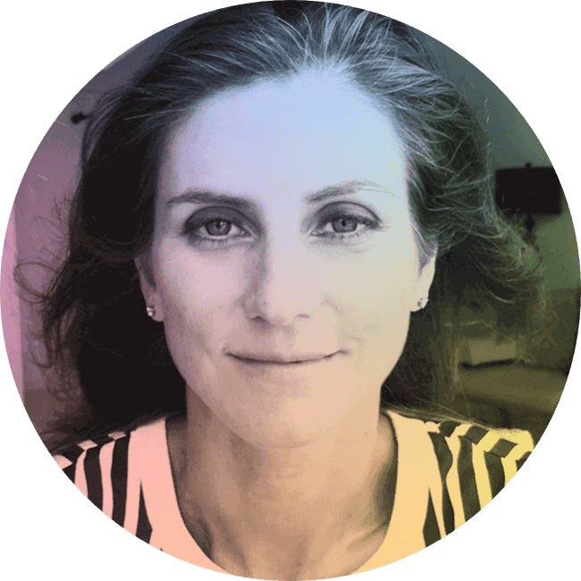 A woman with long, dark hair smiling slightly at the camera, wearing a striped top, in a softly lit room.