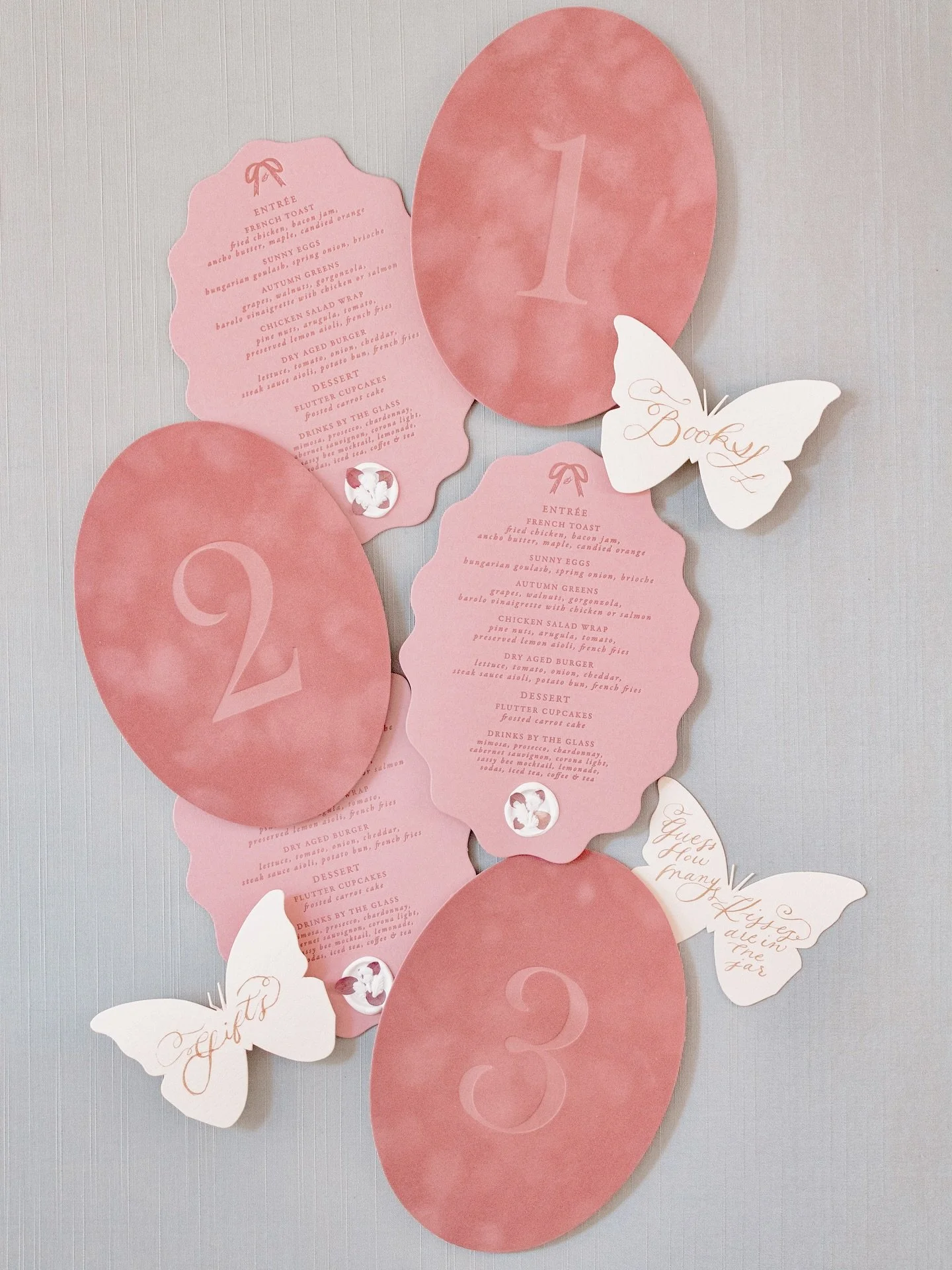 Dusty rose velvet table numbers, tonal letterpress menu cards in a scalloped oval shape with hydrangea pressed wax seals, and custom butterfly shaped table cards in antique gold calligraphy for a baby shower 🎀 

#stationerydesigner #design #statione